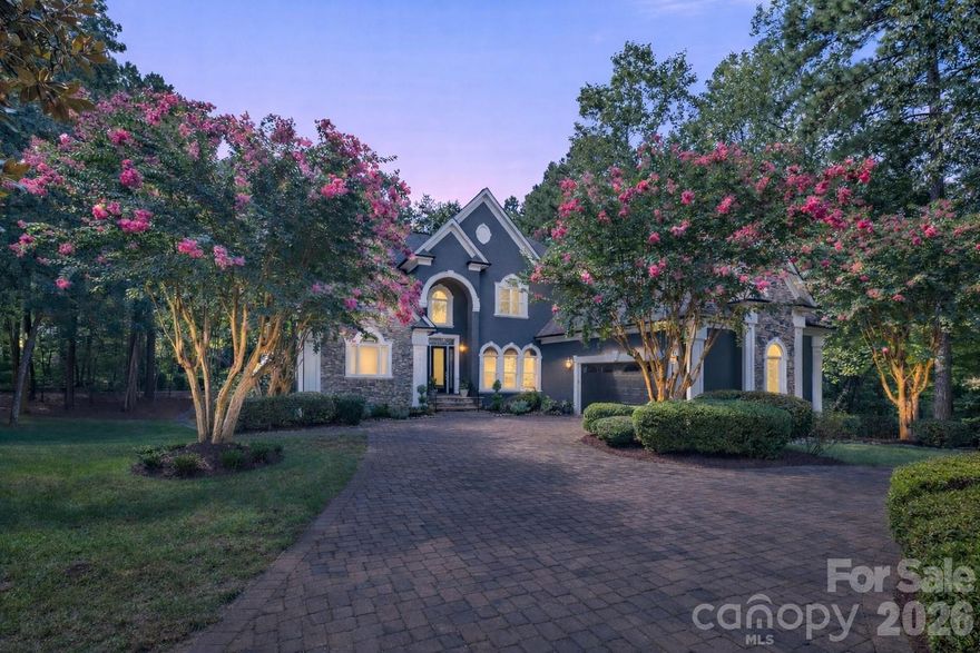 Welcome to an exceptional Lake Norman residence where refined luxury meets effortless lake living. Perfectly positioned within the highly sought-after gated community of Northview Harbour, this remarkable home offers a rare combination of privacy, craftsmanship, and lifestyle—complete with your deeded boat slip just steps away along a semi-private wooded path.

Set on a serene cul-de-sac lot of just over an acre, the home is surrounded by mature trees and thoughtfully designed landscaping, creating a peaceful retreat while remaining moments from the water. With more than 8,500 square feet under roof, including over 1,200 square feet of covered verandas, the property was designed for both grand entertaining and relaxed everyday living.

At the heart of the home lies a stunning open-concept living space anchored by a truly spectacular kitchen. Completely reimagined with luxury in mind, the kitchen showcases custom cabinetry, premium stone countertops, and a generous center island designed for gathering. Top-of-the-line appliances, designer lighting, and exquisite finishes elevate the space, while oversized aquarium-style windows frame tranquil wooded views and flood the home with natural light. The kitchen flows seamlessly into the expansive dining area and great room, where soaring 10-foot ceilings, intricate millwork, wide-plank hardwood flooring, and a statement fireplace create a sophisticated yet welcoming atmosphere.

The main-level owner’s suite serves as a private sanctuary, offering generous proportions and a beautifully appointed spa-inspired bathroom featuring dual vanities, luxury stone finishes, a soaking tub, and an oversized tiled shower. A custom walk-in closet provides abundant storage with a boutique-style feel.

Upstairs, three spacious bedrooms, a versatile loft with hardwood flooring, and a bonus room that opens onto the upper veranda provide flexible living spaces ideal for family or guests. Each room has been thoughtfully designed to balance comfort, functionality, and architectural character.

The walkout lower level transforms the home into a true multi-generational estate, offering a complete second living quarters ideal for extended family, in-laws, or older children seeking their own private space. This level features a full kitchen, dining area, and living room, along with a game room and expansive recreation space perfect for gatherings or entertaining. A nearly 500-square-foot workshop with both interior and exterior access offers endless possibilities for hobbies, woodworking, or additional storage.

Throughout the home, every detail reflects thoughtful craftsmanship and refined design. All bathrooms have been professionally updated with luxury finishes, custom window treatments, elegant lighting selections, and meticulous millwork create a sense of sophistication.

The exterior is equally impressive. A striking brick paver circular driveway welcomes guests with timeless elegance, while multiple covered verandas overlook the wooded backyard—perfect for morning coffee, sunset cocktails, or hosting friends and family. Flowering crepe myrtles and mature landscaping enhance the natural beauty of the property while maintaining privacy and tranquility.

Residents of Northview Harbour, one of Lake Norman’s premier gated communities, enjoy access to resort-style amenities including a clubhouse, pool, tennis courts, playground, walking trails, and a private boat launch. Just steps away to your deeded boat slip, —one of only eight in this section—provides effortless access to the lake while maintaining an exclusive and peaceful setting.

This extraordinary property represents a rare opportunity to experience Lake Norman living at its finest, where elegant design, thoughtful renovations, and an unmatched location combine to create a home that is as impressive as it is inviting. A place where every day feels like a retreat—and where the lifestyle is just as remarkable as the home itself.