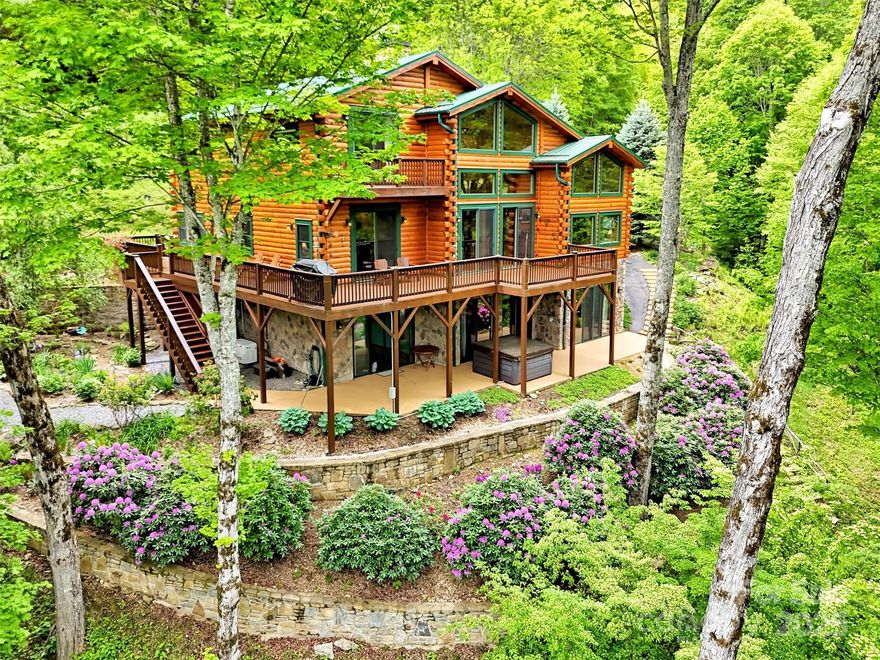 Exquisite Log Home Retreat on 13.21 acres in the gated mountain community of Villages of Plott Creek.  
Escape to peace, privacy & breathtaking beauty with this stunning log home, surrounded by views, vibrant gardens, paths, rock waterfall, all in a "parklike" setting. This property offers the perfect blend of rustic elegance & refined architecture. The home boasts soaring ceilings, warm woodwork throughout & expansive windows that frame mountain views & lush landscaping. Open floorplan,floor to ceiling wood burning fireplace on main level & large laundry room. 3 bdrms, 4.5 baths, including 2 ensuites, with the primary on the main level. Primary ensuite has a gas fireplace & deck access. Lower Level has a spacious family room with wood burning fireplace. PLUS there are TWO bonus rooms for office/bedrooms AND a studio or workshop. Soak in the hot tub, under the stars, after a long day! Meticulously maintained & recently stained. Full house generator ensures peace of mind in any season.