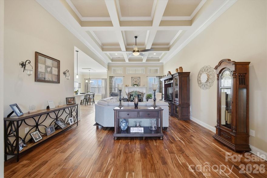 This gorgeous home blends timeless style with quality craftsmanship. The open-concept great room boasts a dramatic coffered ceiling, rich Exotic Acacia hardwood floors, gas fireplace and plenty of natural light. The living area flows easily into the kitchen, which offers soft-close cabinetry, generous counter space, a large center island, stone flooring and chic pendant lighting. The dining room features graceful arched openings, crown molding, and a tray ceiling, perfectly connected to the main living spaces. The primary suite is a private haven with a tray ceiling, Exotic Acacia floors, a custom tile walk-in shower with stone accents, and a decorative mosaic inlay. A split-bedroom layout offers extra privacy, with a shared bathroom featuring dual access. Spacious bedrooms enjoy natural light, ceiling fans, and ample closets. Upstairs, a large bonus room can serve as a gym, playroom, office, or multi-generational space. Outside, the curb appeal shines, complemented by a spacious crawlspace over 5' tall for stand-up access, great storage, and block pier support with vapor barrier coverage. The double car garage has extra storage space for a riding lawn mower and holiday decorations.  Beautifully maintained and thoughtfully designed, this home offers comfort, style, and quality in every detail. The property lines run beyond the black rod iron fencing on both sides. Please see approximate property lines in photos.