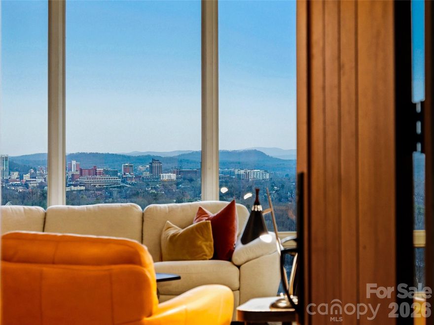 The view is immediate—and unforgettable. From the moment you step inside, downtown Asheville unfolds below you, framed by layers of Blue Ridge Mountains that shift with the light from sunrise to sunset.
Designed by noted architect Bill Ashe to live in harmony with its setting, this home captures the panorama from nearly every room, filling the interiors with natural light and an ever-present sense of place. In the main living areas, floor-to-ceiling windows in the living and dining rooms create a dramatic backdrop—blurring the line between indoors and out while seamlessly connecting to the open kitchen for effortless everyday living and entertaining.
Expansive covered and open-air terraces extend the experience outdoors—perfect for morning coffee above the city, golden-hour gatherings, and evenings under a painted mountain sky.
The main level offers true ease of living with a bright, open floor plan anchored by a spacious kitchen featuring a gas range, generous prep space, and a peaceful view over the landscaped gardens. A butler’s pantry and dedicated kitchen office add thoughtful functionality without compromising flow.
The primary suite is a private sanctuary on the main level, opening to its own deck and offering two walk-in closets and a spa-inspired bath—where even the soaking tub is positioned to take in the mountain backdrop.
A richly appointed library or media room with custom built-ins, a garden-access office, and a large laundry room complete the main level.
Upstairs, two bedrooms, an office with built-ins, and a generous family room provide comfortable separation for guests, while additional flexible space adapts easily to your needs.
Set on a private, beautifully maintained homesite, the level fenced garden, greenhouse, and ideal southern exposure create a rare combination of usability and beauty—enhanced by solar power for modern efficiency.
A large two-car garage with a third bay accommodates a sports car, a golf cart, or recreational gear, and offers convenient access to the main level.
All of this, just minutes from downtown Asheville—yet a world apart.
A home defined not just by its views, but by how it makes you feel living in it.