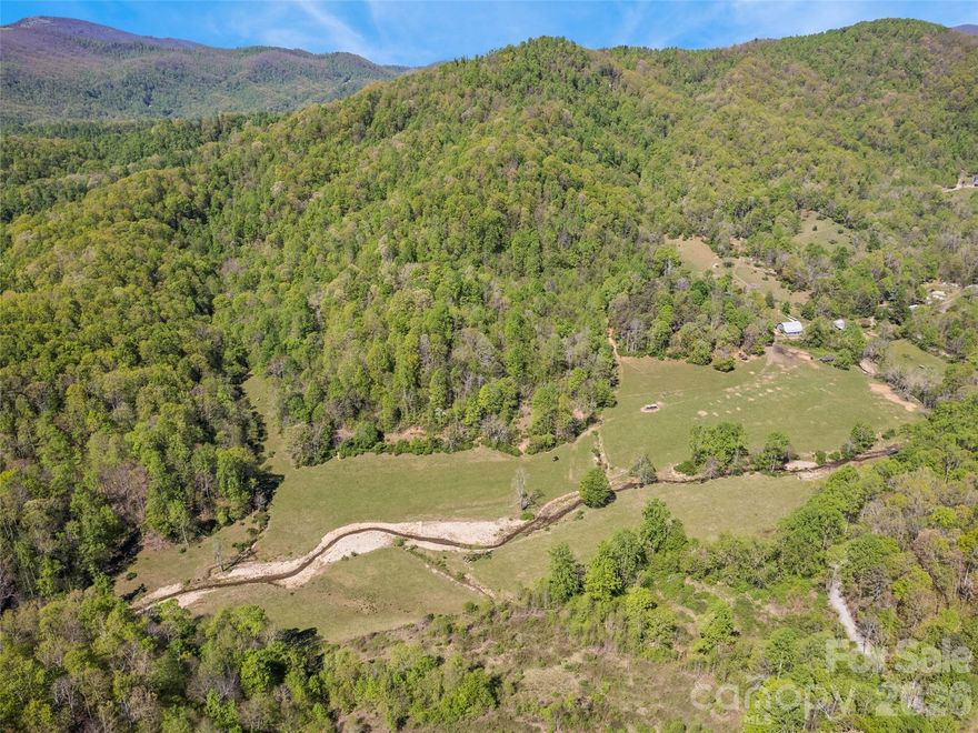 A rare opportunity to steward a multigenerational Western North Carolina farm encompassing approximately 183.73 acres in Buncombe County. Held within the same family for more than a century, this remarkable legacy property reflects deep agricultural roots, abundant natural resources, and a history of careful land stewardship—offering a unique combination of privacy, scale, and authenticity. The landscape is both diverse and functional, featuring open pasture, gently rolling terrain, and expansive wooded acreage, all connected by an established network of internal roads and trails. Water is a defining and exceptional feature of the property, including a private lake/pond, a natural branch flowing behind the farmhouse, and multiple springs and waterways originating from the mountain. The owner has made thoughtful enhancements over time, including the construction of a state-inspected bridge and the creation of small waterfalls designed to support and enhance the natural fish habitat, contributing to both the beauty and ecological vitality of the land. The farm has a long-standing organic, no-chemical history, making it particularly well-suited for sustainable or regenerative agricultural practices. Improvements include a circa 1949 farmhouse, a barn with a concrete foundation, and multiple cabins and outbuildings, including one recently completed post-flood by Amish craftsmen—providing a functional base for continued agricultural use, equestrian pursuits, or the creation of a private mountain estate. Rich in heritage, the property includes, two documented 1800s homestead sites, and a legacy of supplying agricultural goods to the first Ingles store in Asheville. These elements underscore the property’s longstanding role within the region’s agricultural history. The property is enrolled in an agricultural and forestry deferred tax program established in 2019, offering favorable tax treatment for qualified use. This is a distinctive offering for buyers who value land stewardship, historical continuity, and the opportunity to carry forward a generational farm. Seller prefers a single-tract conveyance. Post-closing possession may be requested for a limited period to facilitate transition.