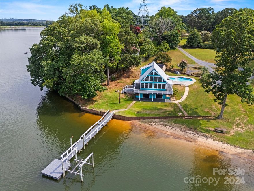This one of a kind, A-frame, waterfront home sitting on the main channel of Lake Wylie w/ no HOA is looking for its new owners to come in make it their own. Step in to tons of natural light flowing in through the wall of windows lighting up the wide plank oak floors running through the open-concept living room & kitchen boasting an oversized island topped w/ river rock granite. The main floor also has 2 BR's w/ bamboo flooring, cedar closets & a full bath. Upstairs, the primary BR is an enclosed loft with a full bath, 2 cedar closets & bamboo flooring. Downstairs, the walk-out basement is spacious w/ potential to have more living space or rec room. There's also a washer/dryer hook up & plumbing for a full bath or kitchenette. Sliding glass doors lead to a covered deck & short walk down to the permitted dock w/7000 lb boat lift w/remote. And don't miss the large tiki bar overlooking the concrete patio with heated in-ground pool, palm trees, wired shed, wrap around deck, & sandy beach.