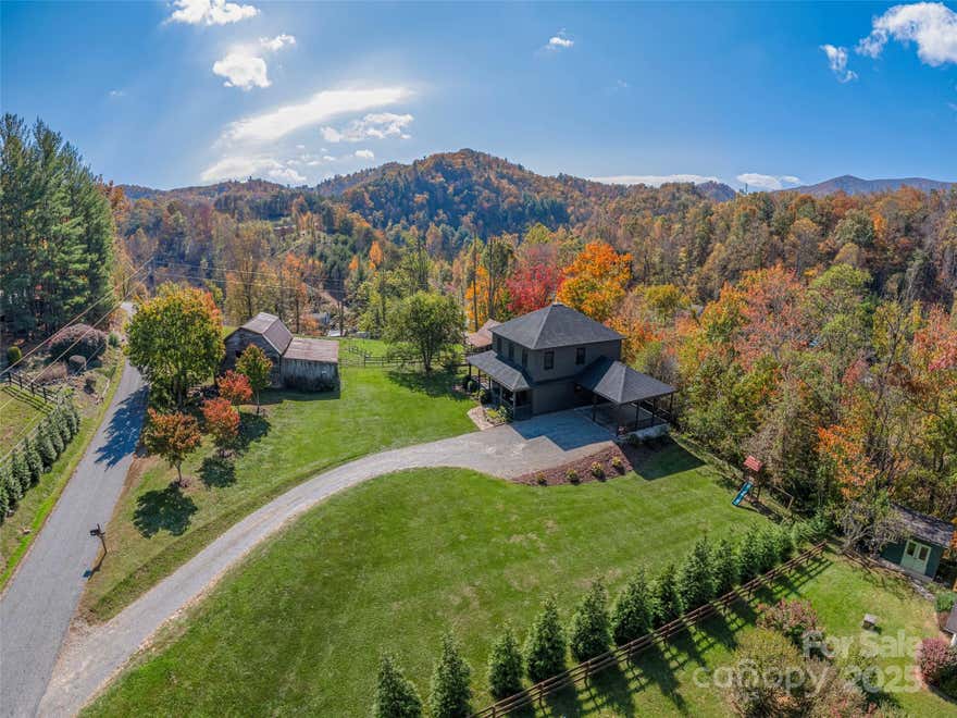 Welcome to Frazier Road-your mountain escape in the Lake Logan community, just 13 minutes from downtown Waynesville and 25 minutes from Asheville. This 3-bedroom, 2.5-bath modern farmhouse sits on nearly 4 acres of fenced, usable land surrounded by long-range mountain views and peaceful privacy. Step inside to an inviting open floorplan filled with natural light, wide-plank wood floors, and warm, modern finishes. The spacious great room features a stone fireplace with wood-burning insert, creating the perfect gathering spot for family or friends. The updated kitchen boasts custom cabinetry, a large center island, stainless steel appliances, and ample counter space for entertaining or meal prep. The main floor features a bonus room which offers endless flexibility for a home office, playroom, or guest suite. The primary suite includes a spa-inspired bath with dual vanities, wood countertops, and updated accents. Outside, enjoy the covered wraparound porch overlooking the mountains, or retreat to the fenced pasture, garden area, and historic barn—ideal for animals, storage, or a future workshop. A separate guest cottage provides additional living space, home studio, or creative getaway complete with new flooring and mini-split HVAC. Located over the mountain from Waynesville and Canton, this property blends mountain serenity with accessibility-perfect for a full-time residence, second home, or vacation retreat. Experience peaceful mountain living at its finest in this move-in-ready Lake Logan retreat.