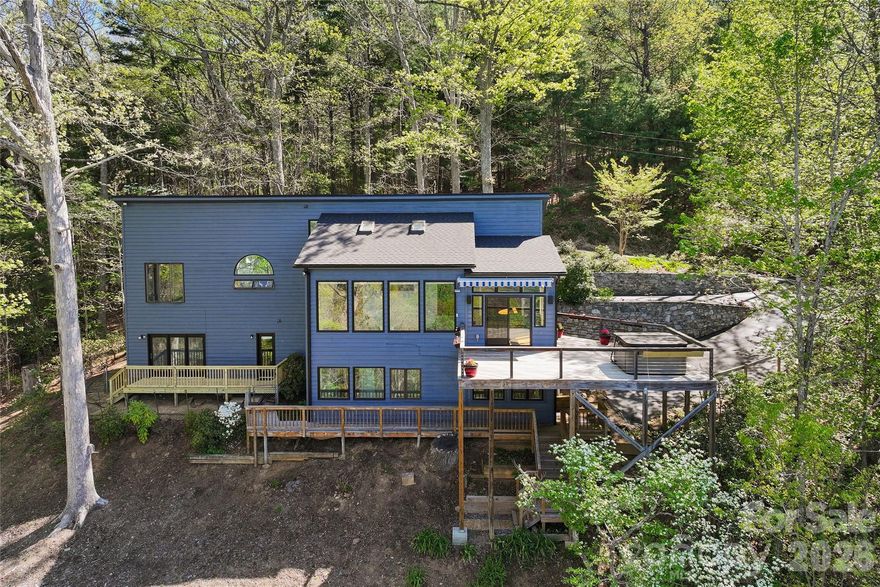 Perched above Asheville, this inviting mountain home captures sweeping views of the Blue Ridge Mountains and the city below. Expansive windows across the main level fill the home with natural light while framing the ever-changing scenery, creating a warm and comfortable living environment. Designed for easy main-level living, the open floor plan features a spacious living room that flows seamlessly into the kitchen and dining area—ideal for both everyday living and entertaining. A bright sunroom offers a peaceful, year-round retreat. The primary suite is privately situated and features a spa-like bath with a jetted tub, large walk-in shower and abundant natural light. A main-level laundry room adds to the home’s convenience. Outdoor living is equally impressive, with expansive decks that provide ample space to gather, relax and take in the views toward downtown Asheville. The lower level offers a generous bedroom/bonus room along with an additional bedroom, providing flexibility for guests, a home office, or recreation space. Additional highlights include a new roof, a quiet dead-end setting offering exceptional privacy, and three separate driveways for ample guest parking. Offering the additional lot below to protect your views. Ideally with easy access to Merrimon Avenue, downtown Asheville and the Blue Ridge Parkway, this home offers tranquility and convenience. House and additional lot in this listing. Unique tax advantage as city taxes apply to the lot, while the home is county taxed, resulting in reduced overall property taxes. Combining stunning views, thoughtful design and an unbeatable location, this property delivers the best of Asheville mountain living.