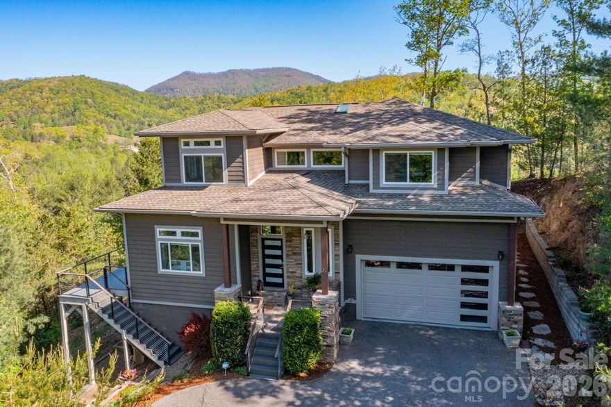 Experience elevated mountain living at its finest at 36 Spy Pointe Lane, where panoramic, long-range views take center stage from nearly every room. Designed to showcase the surrounding beauty, expansive windows—including a striking picture window in the upstairs hallway—fill the home with natural light and uninterrupted vistas.

The main level offers an open, flowing floorplan with bamboo flooring throughout and a gas log fireplace anchoring the living room. A wall of windows frames breathtaking views, creating a seamless connection between indoor comfort and the natural landscape. The chef’s kitchen is both stylish and functional, featuring quartz countertops, tile backsplash, custom cabinetry, a gas range with hood, a walk-in pantry, and a spacious island with breakfast bar. The adjoining dining area opens to a screened porch and deck, perfect for enjoying sunrise coffee or evening sunsets.

A main-level bedroom with deck access and nearby full bath adds flexibility for guests or main-floor living. A mudroom connects to the oversized two-car garage with dedicated workshop space.

Upstairs, the primary suite is a private retreat with its own deck and sweeping mountain views. The luxurious ensuite bath includes a dual vanity, soaking tub, large tiled shower, water closet, and walk-in closet. Additional living spaces include a family/bonus room, office with adjoining half bath, laundry room, 1 bedroom and 1 sleeping/bonus room (home is on a 3 bedroom septic but lives like a 4 bedroom).

Outdoor living is enhanced by beautifully tiered gardens and multiple spaces to relax and entertain. With a newly encapsulated crawlspace, central vacuum, and new HVAC (2025), this home blends refined comfort with thoughtful upgrades. Ideally located between Fletcher and Fairview, just 15 minutes to Asheville and convenient to shopping, dining, and outdoor adventure.