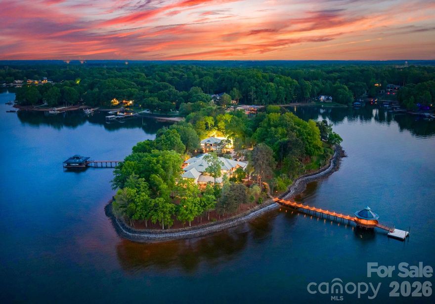 Designed by renowned architect Harry Schrader, Merancas Island is an extraordinary private island standing as one of the most significant residential offerings ever to come to market in the Carolinas. Spanning 4.5 pristine acres along Lake Norman’s shoreline, this estate delivers a resort lifestyle with no equal. Custom architectural details, bespoke lighting, and timeless design define every corner of the 14,317-square-foot residence. 

A gated entry winds through lush tropical grounds past palm trees, sculpture gardens, the guest house, and tennis court before arriving at the primary residence, where breathtaking lake views greet you from every room. A covered pavilion entry path flanked by a tranquil pond leads to curved doors with elegant colored glasswork, opening into a foyer of immediate distinction. Soaring 20-foot ceilings and a refined stone fireplace set the tone for the craftsmanship found throughout. Elevator access to the upper level and attic is positioned just off the entry hall.

The great room is the heart of the home, featuring a 25-foot ceiling, lake views on three sides, and expansive windows that dissolve the boundary between interior and exterior. A gas fireplace anchors the space as doors flow out onto multiple patios overlooking the water. The kitchen features a generous island, gas cooktop and ovens, granite countertops, and a full butler's pantry, all complemented by a sunny breakfast area with lake views. The dining room offers architectural ceiling details, a stone fireplace, and a custom light fixture by Schrader, with direct access to a screened outdoor patio. A dedicated wine room with stone finishes, custom racks, and glass display cabinetry sits nearby.

One of the home's most remarkable amenities is the enclosed indoor pool, clad in Tennessee Field Stone and cedar walls beneath a cedar ceiling with skylights and integrated plant walls. A full bath with sauna complements the pool area. Adjacent, a sun-filled flex room with plantation shutters and a glass wall peering into the pool space serves equally well as a bonus guest suite, office, or playroom. A private executive office features custom built-ins and a sliding panel connecting to the crafting room beyond, a generous creative space anchored by a large center island. Additional main-level spaces include a storage room, a full bath, a powder room, and a drop zone from the three-car garage.

The upper level is anchored by the exceptional primary suite, featuring a custom platform bed with integrated bookshelves, a fireplace, and a hidden bookcase door that opens to a reading loft with a spiral staircase to the great room, making this space genuinely one of a kind. The primary bath offers dual vanities, a soaking tub, a custom stone and wood shower, and two walk-in closets with glass display cabinets. A private terrace overlooks the water from the bedroom.
Two guest bedrooms offer lake views and an ensuite bath, served by an additional shared hall bathroom. The theater room delivers a full entertainment experience with a pool table, wet bar, and projector system. The children's playroom is a world of its own, a hand-painted mural wraps the walls and ceiling, built-in beds with trundles, and an adjacent wet room handles every art project and lake-day cleanup with ease.
The guest house offers a recently updated retreat with an open-concept living and kitchen area, two bedrooms, a shared bath, and its own three-car garage. Outside, stone walkways wind through the island, past a fenced tennis court, two docks with boat lifts and a covered gazebo, a sandy private beach, a shed, and a dog run. 

Ideally situated less than 30 minutes from Uptown Charlotte with convenient access to major roadways, Merancas Island places you at the heart of everything Lake Norman has to offer, from world-class dining, boating, waterfront recreation, to a vibrant social scene. This is lake living at its absolute finest.