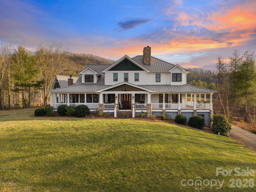 Framed by sweeping mountain views and the beauty of Reems Creek Valley, this one-of-a-kind Contemporary Farmhouse offers an extraordinary take on mountain luxury. Timeless craftsmanship is evident throughout, from the wrap-around porch and reclaimed wood, to the stonework and architectural details gathered from around the world, all set on 5.34 private acres. An unforgettable mountain retreat minutes from downtown Weaverville and Reems Creek Golf Course.
The dramatic two-story great room anchors the home with a floor-to-ceiling wood-burning stone fireplace, reclaimed stained-glass accents, and French doors opening to the rocking chair porch.
The chef’s kitchen is beautiful and functional with a large island and vented gas range, dual ovens, a farmhouse apron sink, walk-in pantry, and custom wet bar. Reclaimed tin ceiling tiles and wood beams add texture and charm, while the spacious dining area and cozy sitting alcove and fireplace make the space perfect for gathering and entertaining.
The primary suite on the main level has its own gas fireplace, ensuite bath, and a thoughtfully designed walk-in closet with built-ins. The spa-like bath features radiant heated tile floors, a soaking air tub, dual vanities, and a walk-through stone and tile shower with multiple jets.
Upstairs, look down on the great room from the balcony and enter a private guest suite with a sitting area, wet bar, fireplace, ensuite bath and private covered porch. Two additional bedrooms and flexible living spaces complete the upstairs. The lower level provides more room to spread out, featuring an oversized entertainment room, wet bar, full bath, and additional flex space or home gym.
Outdoor living is every bit as inviting, with a covered wrap-around porch designed to capture sunrise, sunset, and mountain views, a custom stone firepit, and three acres of cleared pasture ideal for horses, a mini farm, or future expansion.
More than a farmhouse, this is a legacy property that will be treasured for generations to come.