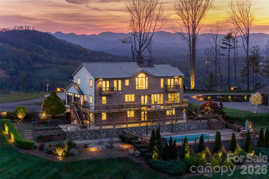 Welcome to 83 Cozy Mountain Lane, set on approximately nine private, gated acres in the Blue Ridge Mountains and offering a rare blend of refined mountain living, expansive scale and exceptional 360-degree views. Ideally just minutes from downtown Weaverville and approximately 15 minutes to Asheville, the property provides convenient access to dining, arts and culture while remaining close to outdoor destinations including the Blue Ridge Parkway and Pisgah National Forest. Spanning approximately 4,963 square feet, this four-bedroom, four-bath residence is thoughtfully positioned to capture sweeping long-range mountain views from the moment you enter the driveway and carry through nearly every room.  A striking great room with a stone gas fireplace sets the tone upon entry, seamlessly flowing into a light-filled living area framed by expansive picture windows that capture sweeping mountain views. From here, go out onto the Trex deck with a gas fire pit, overlooking a resort-style in-ground pool, patio and custom stone fire pit, an ideal setting for elevated, year-round entertaining. The kitchen serves as the heart of the home, featuring a suite of KitchenAid appliances, including a wall oven, microwave, five-burner gas cooktop and refrigerator, complemented by a Bosch dishwasher. Leathered granite countertops, a large island, stainless apron-front sink and under-cabinet lighting balance function with understated luxury. A dedicated office, integrated speakers and a well-appointed mudroom and laundry suite complete a main level that’s as functional as it is refined. Upstairs, the primary suite offers a private retreat with vaulted ceilings, transom windows and a Juliet balcony overlooking the pool and surrounding mountains. The spa-inspired bathroom features a freestanding soaking tub set before a picture window, dual marble vanities, a spacious walk-in shower with pebble stone flooring and refined stone accents. Two additional guest bedrooms, full bath and a loft living area complete the upper level. The lower level expands the home’s versatility with full secondary living quarters, including a recreation room, living room with wood-burning stove, complete kitchen with stainless appliances, dining area, guest bedroom and full bath. Dedicated systems, including dual water heaters and mini-split climate control, make this space ideal for guests, multigenerational living or extended stays. A detached, fully climate-controlled outbuilding/garage adds further flexibility. In addition to generous garage space, the structure includes a dedicated office, ideal for remote work, fitness or creative use, complementing the property’s overall sense of scale and privacy. Beyond the home, the property unfolds into a private, gated mountain estate defined by rare, gently sloping ridge-top land. The approximately nine acres are usable and visually striking, offering open areas suited for recreation, gardens or expanded outdoor living, all framed by panoramic long-range views. Offering a rare combination of acreage, privacy, proximity and commanding mountain views, 83 Cozy Mountain Lane is designed for everyday living and exceptional entertaining.