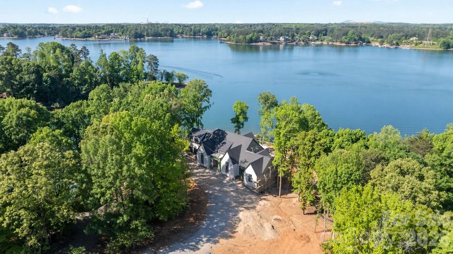 Set on a rare 1.42-acre waterfront lot with over 500’ of Lake Norman shoreline with big open water main channel views. This new custom estate built by CTR Homes and designed by Sara Lynn Brennan Interior delivers a seamless blend of architectural elegance, cutting-edge smart living, and resort-style comfort, all designed for those who expect more from every detail. From the moment you arrive, the home’s modern exterior, expansive driveway, and 3-car garage with epoxy floors establish presence. Inside, soaring ceilings, hardwood floors, and curated finishes create a refined yet inviting atmosphere that immediately feels like home. The heart of the home is a stunning open-concept living space framed by bronze Andersen windows that flood the interior with natural light and capture uninterrupted Lake Norman waterfront views. The designer kitchen is both a showpiece and a chef’s dream, featuring marble countertops, a 48-inch Thermador gas range, top-tier appliances, and a fully equipped scullery with a built-in app-controlled coffee system, second dishwasher, prep sink, microwave, fridge drawer and freezer drawer. The main-level primary suite is a private retreat designed for comfort and indulgence, complete with a boutique-style custom closet featuring its own island, chandelier, and in-suite washer and dryer. The spa-inspired primary bath elevates daily living with heated floors and programmable shower settings, delivering a personalized luxury experience every day. The lower level fully finished walk-out basement transforms into an entertainer’s dream and a private guest haven. With three additional bedrooms, 2 full baths, a media room, fitness room, rec room, custom bar, and dedicated lake bathroom, every inch of space is intentional and elevated. A climate-controlled wet storage area ensures effortless lake living year-round. Step outside and the lifestyle truly begins. Enjoy a heated pool and spa, outdoor gas grill, and fully fenced backyard, all designed for both intimate evenings and large-scale entertaining. Your private waterfront experience is complete with a brand-new dock and pier with boat lift, offering direct access to the best of Lake Norman boating. This home is fully equipped with indoor-outdoor surround sound, touchscreen lighting controls, security cameras, and two tankless water heaters, blending luxury with smart efficiency. Located near Lake Norman State Park, marinas, golf courses, and top dining destinations, this property offers both privacy and convenience, with easy access to Mooresville and Charlotte. No compromises. Just elevated living.