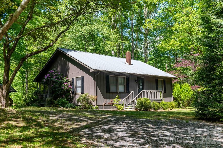 Tucked into the gentle folds of near hills at the feet of the Black Mountains, this quiet retreat unfolds across nearly six acres of pastures, woods, and cleared garden land. A robust creek marks the property’s beginning, its voice a constant, soothing presence that reaches the home and lingers in the air. Tiny streams thread through the acreage, whispering through the grass and trees.

At the heart of the land sits a lovely two-bedroom home, where a wood stove offers deep winter warmth and a mini split provides summer comfort. The kitchen is decently sized, well-suited for putting up the garden’s harvest or simmering a slow meal while the creek runs beyond the window.

One section of the property is shaded by enormous old trees, standing like patient elders beside a very old but still sturdy barn, weathered, honest, and full of stories.

The true soul of the home, however, is the screened back porch. From here, the view rolls out across the yard, over the stream, and off toward the semi hidden hills. It is the kind of place where morning coffee lasts an hour and evening fireflies keep you company.

Just steps away, a separate one-bedroom, one-bath cabin offers its own magic: a large sliding door frames the same sweeping vista of stream, yard, and far hills, bringing the outside in. Whether as a guest retreat, an artist’s studio, or a quiet escape, it mirrors the main home’s best feature: an unbroken connection to this peaceful, water-song land.