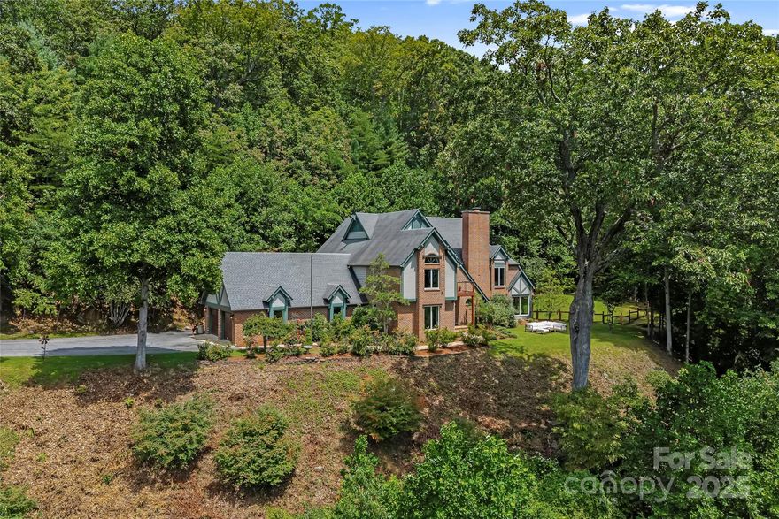 Discover breathtaking layered mountain views at this elegant brick Tudor, just 4.5 miles from downtown Asheville in sought-after Sondley Estates. Enjoy panoramic views of the Pisgah Mountains the moment you arrive and throughout the home, including the luxurious primary suite. This remarkable residence features a dramatic two-story vaulted foyer, a spacious family room, and an open-concept chefs kitchen with high-end designer appliances. A rare flat, fenced yard offers full privacy and includes an outdoor kitchen, perfect for year-round entertaining. The primary suite is a private retreat with a soaking tub, walk-in shower, generous 150 sq ft closet, and separate office. An oversized 4-car garage adds storage and convenience. Priced below recent appraisal, this home is an exceptional value in one of Asheville's most established neighborhoods. A true mountain sanctuary just minutes from the heart of the city!
