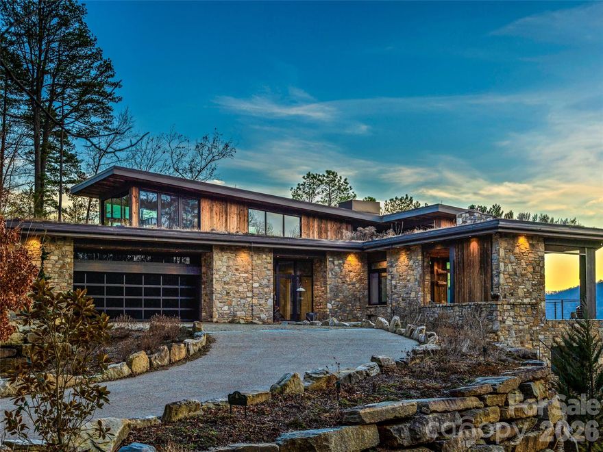 Located in the Asheville Metropolitan Area and nestled on a sweeping bend of the French Broad River, 112 Moon Shadow Lane is a stunning mountain-modern retreat designed by renowned architect Platt. Situated within the coveted gated community of French Broad Crossing, this sanctuary is celebrated for its privacy and conservation. Designed to harmonize with its surroundings, with expansive river and mountain views, walls of glass, provide an immersive and tranquil living experience.


The interior showcases natural materials and meticulous craftsmanship at every turn. Soaring reclaimed hemlock ceilings throughout, stone accents and sculptural steel fireplaces infuse warmth and texture, while custom cabinetry and refined finishes elevate everyday living. The great room seamlessly flows into a chef’s kitchen crafted for both artistry and functionality, featuring grain-matched cabinetry, leathered granite concrete countertops, premium appliances and a dedicated wet bar—perfect for gatherings that extend into the evening.


Indoor and outdoor living blend effortlessly here. A retractable screened porch with a wood-burning fireplace provides an outdoor retreat, while several terraces and patios provide front-row views of the river below. The main-level primary suite sanctuary features its own terrace overlooking the water and a spa-inspired bath.


Versatile living spaces include a loft office with river vistas, guest or fitness suite and a lower-level recreation area seamlessly connecting to a full-length patio and bocce court. Thoughtful amenities, including a wine room, secondary wet bar, lower-level laundry, in addition to the main level laundry, and multiple en-suite bedrooms.


Surrounded by meticulously curated native landscaping, stone pathways, and serene outdoor nooks, this property is both tranquil and sophisticated. While it feels secluded, it remains convenient to Marshall, Hot Springs, Weaverville, and Asheville, offering access to dining, culture and essential conveniences.


In addition to its architectural integrity and natural beauty, this home is equipped with a 3+ car garage, elevator for access to all levels, and a generator and a lightning protection system for peace of mind. 112 Moon Shadow Lane embodies a riverfront lifestyle distinguished by exceptional design, natural beauty and lasting value—a rare opportunity to own a legacy property where craftsmanship and nature coexist in perfect harmony.