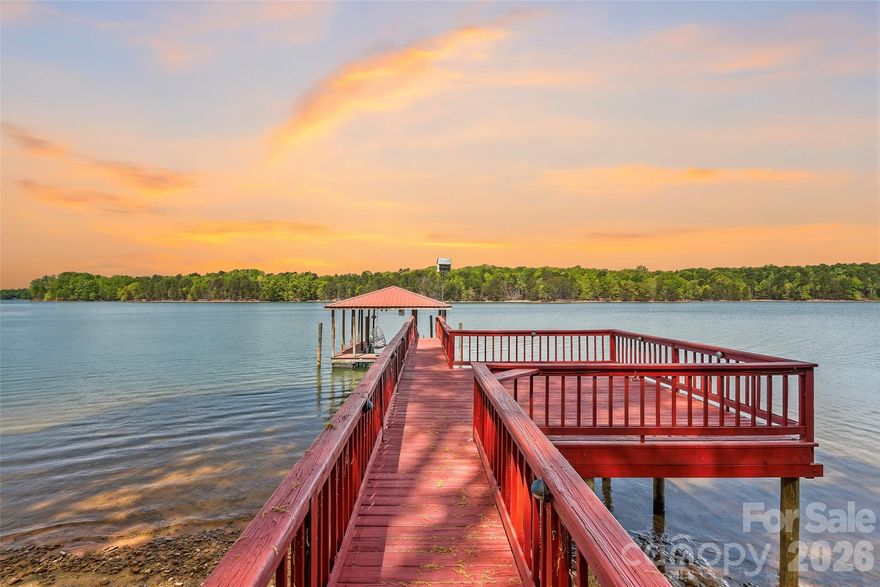 Located within the exclusive Hawkes Bay neighborhood, this exceptional custom full-brick waterfront home offers nearly 400 feet of pristine Lake Norman shoreline with year-round deep water and breathtaking wide-water sunset views from almost every room. Ideally situated just off the main channel, the property provides a rare blend of privacy, protected waters, and convenient lake access, offering the ultimate setting for relaxed yet refined lake living. The expansive waterfront playground features two private beaches, a covered boat slip, boat lift, floating dock, and two jet ski docks, offering effortless enjoyment on the lake for all water enthusiasts. The main level showcases a spacious primary suite highlighted by an updated spa-style bath with soaking tub and a walk-in closet. The large kitchen is beautifully appointed with granite countertops, abundant cabinetry with roll-out drawers, a tile backsplash, and a breakfast bar opening to a bright sunroom, all flowing seamlessly to the expansive wrap-around back deck, ideal for entertaining or relaxing while taking in sweeping lake views. The upper level offers two additional bedrooms, two full baths, a bonus room that may serve as an optional bedroom, and an open loft perfect for an office, media space, or play area. The finished walk-out basement adds flexibility with a large bedroom, full bath, recreation room, and wet bar, along with an unfinished workshop and generous storage areas. Surrounded by a private wooded setting directly across from Lake Norman State Park, the home enjoys a serene natural backdrop while also offering immediate access to miles of scenic walking trails, premier mountain biking trails, and outdoor recreation. Whether it’s a morning hike, an afternoon ride, or simply exploring everything the park has to offer, this location delivers a rare combination of waterfront luxury and outdoor lifestyle, completing a remarkable opportunity that truly represents the finest in Lake Norman living.