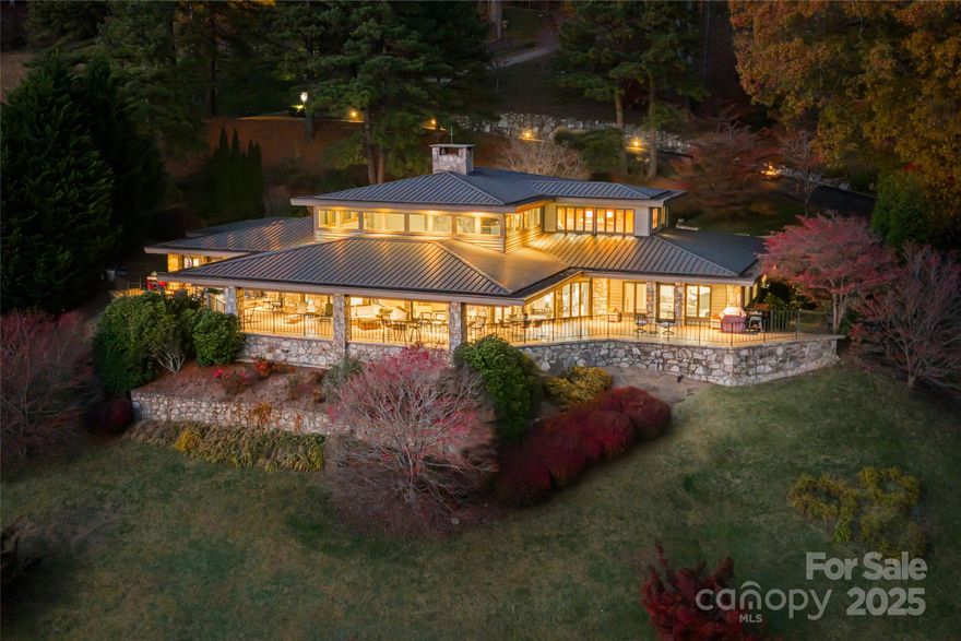 Architectural artistry and refined mountain living come together above the most scenic green at Laurel Ridge Country Club. Positioned over the 11th tee with panoramic mountain, golf-course, and valley views, this contemporary residence offers one of the most striking vantage points in Waynesville. Originally inspired by the Frank Lloyd Wright style, the home was re-envisioned in 2008 to honor clean lines, natural materials, and seamless connection to the outdoors while adding modern comfort and function.

Walls of glass pull the landscape inward, filling the great room with natural light and framing the Blue Ridge like living art. A soaring ceiling, floor-to-ceiling stone fireplace, and striking architectural details create a space that feels both dramatic and deeply welcoming. Just beyond, a wide wrap-around veranda spans the length of the home—an unforgettable outdoor living environment for sunset dinners, weekend entertaining, and quiet mornings overlooking the fairway and long-range ridgelines.

Designed for effortless main-level living, the primary suite provides a peaceful retreat with an adjoining bonus room currently used as a home gym. This space adapts beautifully as a private office, sitting room, Hollywood-style dressing room, or the footprint for a second spa-like bath. The kitchen is supported by both a butler’s pantry and a separate walk-in pantry, ideal for everyday life and elevated entertaining. A distinct everyday entrance and separate guest entrance add sophistication to the home’s sense of arrival.

The upper level functions as a private guest wing with a second primary suite, a large loft, an office, and another ensuite guest room—perfect for extended stays and hosting with ease. Fully zoned HVAC, ample basement storage, an oversized two-car garage, a brick-paver driveway, and extensive exterior lighting reflect thoughtful planning inside and out.

All of this awaits just minutes from historic downtown Waynesville, known for boutique shops, fine dining, galleries, and year-round festivals—and only about 30 minutes from Asheville, a nationally regarded destination for arts, culture, and acclaimed restaurants.  A rare opportunity to own a luxury residence with sweeping mountain and golf-course views, timeless architecture, and one of the most inviting outdoor living spaces in Western North Carolina.