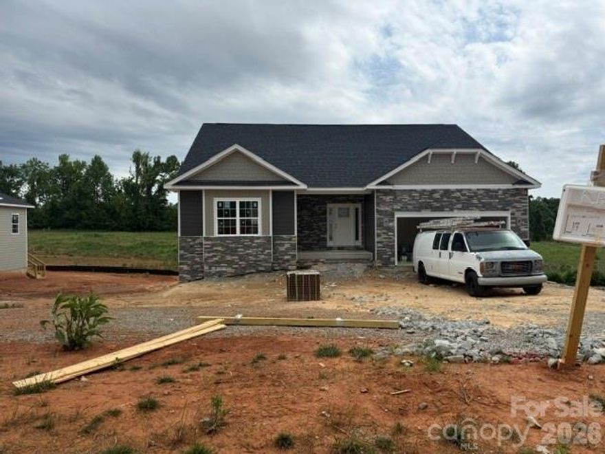 Only $1,000 down to write a contract—don’t miss this exceptional opportunity to own brand-new construction in the highly desirable McNeely Farms community in Mt. Ulla, NC! Situated on a generous 1.05-acre homesite, this home offers the perfect blend of peaceful country living with convenient access to downtown Mooresville, shopping, dining, and I-77 and I-85.This thoughtfully designed one-and-a-half story plan with a fully finished basement offers an impressive 3,878 total square feet of living space. The home features 4 bedrooms, 4 full baths, and a dedicated flex space/office—ideal for today’s flexible lifestyle needs.The main level boasts 3 bedrooms and 2 full baths, along with a spacious open-concept layout. The kitchen is a true centerpiece, featuring quartz countertops, a large center island, tiled backsplash, and a gourmet stainless steel appliance package. Laminate wood flooring flows throughout the main living areas, while the formal dining room is enhanced by elegant coffered ceilings.Upstairs, you’ll find a private office, full bath, and an expansive recreation room—perfect for a media space, playroom, or additional living area. The finished basement further expands your options with an additional bedroom and a large recreation room, ideal for entertaining, a home gym, or guest suite. Walk-out access leads to a patio and a private, level backyard, creating seamless indoor-outdoor living.The primary suite offers a relaxing retreat with a beautifully tiled 5-foot shower. Step outside to enjoy the 16’ x 14’ covered deck overlooking serene surroundings—perfect for morning coffee or evening gatherings.
Exterior highlights include durable Hardie board siding, an upgraded stone package, and the added benefit of no HOA fees. Closing cost paid (except prepaids and points) with use of preferred lender.  Flex cash available to lower interest rate!!
