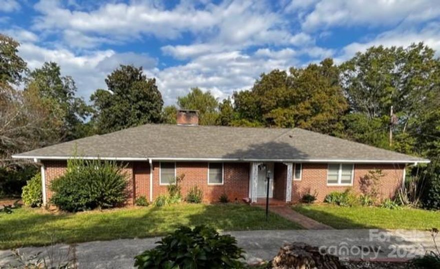 Situated within walking distance to quaint downtown Rutherfordton and a short drive to both Lake Lure and the Equestrian Center, this spacious ranch home offers one-story living with an additional two bedrooms and a full bath in the walk-out basement. The main level features well maintained wood floors, large bedrooms, each with double closets, two living areas with fireplaces and a bright dining room. Enjoy the private, wooded backyard from the enclosed main level porch or brick paver patio on the lower level. The horseshoe driveway wraps around a large flowerbed ready for your green thumb. A second driveway leads to the oversized rear garage and an additional parking area. The kitchen and bathrooms provide an opportunity to showcase the home's vintage character or update style with a few cosmetic projects. New roof and carpeting were just installed and neutral paint added in living and dining.