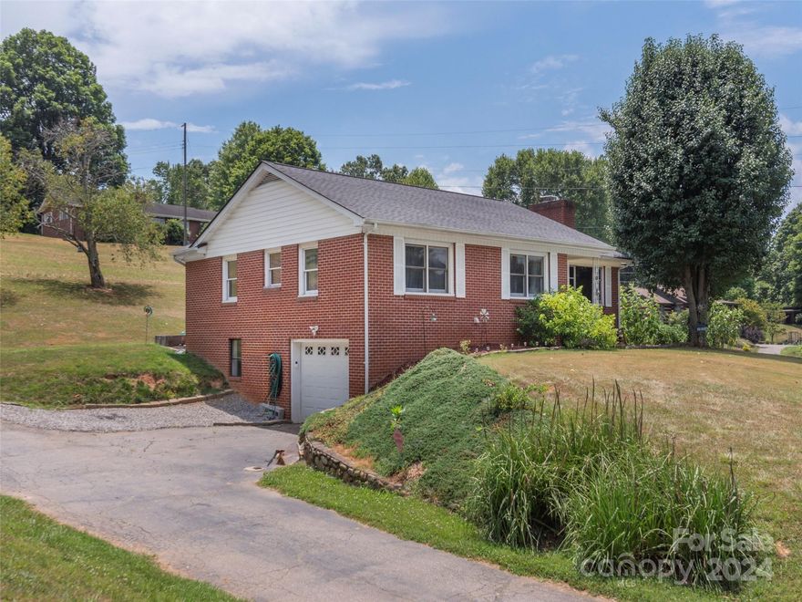 Welcome to this charming brick ranch home nestled on a serene property, offering the perfect blend of comfort and outdoor enjoyment. This inviting home features three cozy bedrooms and one bathroom with ample living room space, including a wood stove. The living room and primary bedroom boasts original hardwood floors. The spacious outdoor area is a true highlight, complete with a fire pit for evenings under the stars and a covered back porch, perfect for relaxing, entertaining, or taking in the mountain views. Inside, you'll find a full basement providing storage or room to expand the living square footage. The one-car garage and large driveway ensures plenty of space for vehicles. Whether you're looking for a comfortable retreat close to town, or a place to create lasting memories, this property offers it all. Don't miss the opportunity to make this beautiful ranch home yours! Easy commute to Asheville and Waynesville.