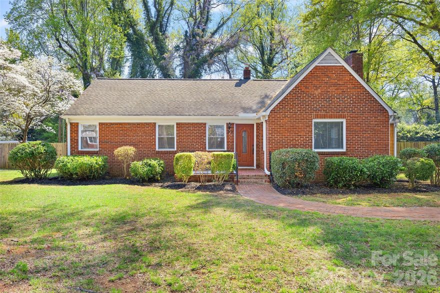 Nestled in Medford Acres, one of Charlotte’s true hidden-gem neighborhoods, this charming all-brick 1950s ranch offers the rare combination of natural beauty, timeless character, and close-in convenience. Tucked beneath a wonderful mature tree canopy and backing to the Evergreen Nature Preserve, the setting feels peaceful and unexpectedly private, yet you are right in the heart of Charlotte with easy access to vibrant Midwood, Center City, shopping, dining, and entertainment. Independence Boulevard is just moments away, making it easy to reach Uptown, SouthPark, Matthews, and the University area. Set on a healthy, flat .37-acre lot and offering approximately 1,394 heated square feet, the property offers both space and serenity in an increasingly rare close-in setting.

An inviting open front porch welcomes you inside, where natural light flows beautifully throughout the home and highlights the warmth and character found in every room. A foyer opens through a casement opening into the living room, where beautiful hardwood floors and a fireplace create an inviting central gathering space. From there, an arched opening leads into the dining room, adding architectural charm and a sense of graceful flow. A square opening connects the dining room to the kitchen, while another arched opening leads from the dining room into the office area, creating a layout that feels both connected and distinct.

The kitchen, an addition clad in cedar shake siding, has been thoughtfully updated and offers a clean-lined modern aesthetic balanced by warm, natural materials. Natural wood tone shaker cabinetry, a paneled dishwasher, stainless steel appliances, mottled gray, black, and white granite countertops, and a custom tile backsplash come together to create a space that feels both stylish and welcoming. Generous in size and filled with natural light, the kitchen also offers room for a breakfast table, making it as functional as it is inviting. Just beyond, a door opens to a large deck overlooking the fenced rear yard — a truly special outdoor space featuring a substantial and beautifully designed koi pond that brings a peaceful, garden-like quality to the property. The flat yard offers ample room to enjoy, garden, entertain, or simply relax and take in the natural surroundings.

The home features two bedrooms and two full baths. The hall bath retains its vintage charm and is in beautiful condition, offering a delightful nod to the home’s era and personality. The renovated primary bath introduces a more modern note, highlighted by a seamless glass shower enclosure with glass on two walls, handsome full-height tile surround, built-in niches, and a striking vertical accent band that adds texture and visual interest. Hardwoods run throughout nearly the entire home, adding warmth and continuity, with the exception of the entry hall and office. The office area features tile flooring and a barn door opening to the laundry closet, while also providing direct access to the rear yard for added flexibility and convenience.

A one-car garage adds practicality, while the neighborhood itself is one of the home’s most special features. Medford Acres is beloved by those who know it for its friendly, grassroots feel, mature trees, and genuine sense of community — a neighborhood where homeowners enjoy one another and where the setting feels tucked away despite being moments from some of Charlotte’s best amenities. Notable updates include a roof replacement in 2015 with architectural shingles, HVAC replaced in 2016 with a gas pack system, and replacement vinyl windows installed at a prior time.

This is a rare opportunity to own a character-filled home on a beautiful lot in one of Charlotte’s most quietly treasured neighborhoods, where preserved natural surroundings, abundant light, established charm, and urban accessibility come together beautifully.
