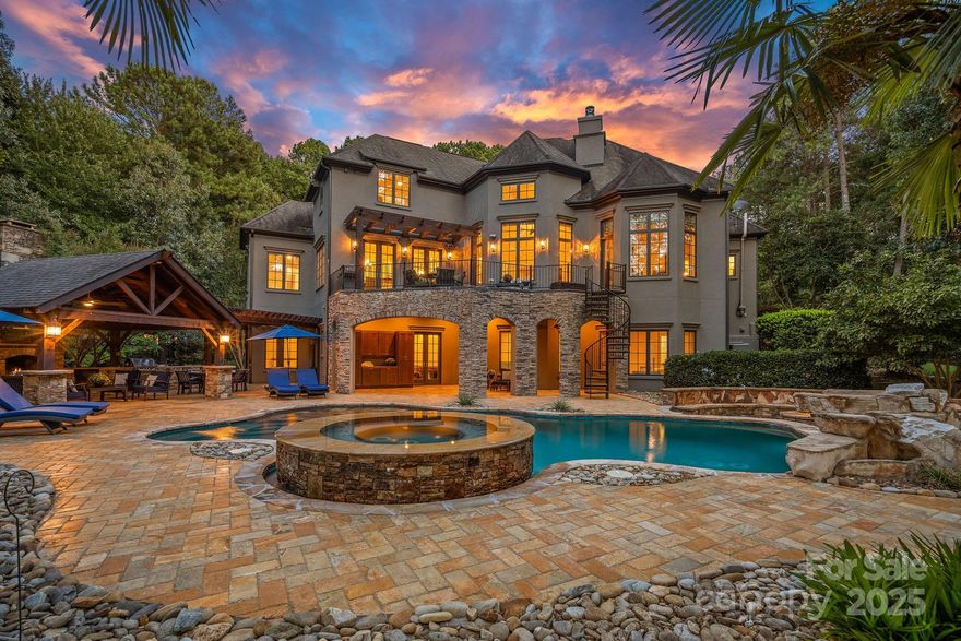 Magnificent 5-bedroom, 5.5-bath waterfront retreat in The Point, showcasing a stucco and stone veneer exterior with a private dock featuring a boat lift and two wave runner ramps, nestled on nearly 2.5 acres of secluded grounds with approximately 425 feet of shoreline. The expansive main level boasts soaring ceilings, modern lighting, and exquisite crown molding throughout. It includes a vaulted-ceiling office, a dining room with wainscoting and tray ceiling, plus a spacious great room with a gas fireplace and coffered ceiling. The kitchen dazzles with brushed gold pendant lighting, honed leathered steel gray countertops, a commercial 48" range, and a generous breakfast area. The primary suite, located on the main level, features a double tray ceiling and a door opening to the patio, accompanied by two guest bedrooms. Upstairs, an additional guest bedroom with a full bath provides extra comfort. The lower level offers a billiard room, family room, gym, two more bedrooms, ample storage, and a lake garage with a workshop. Outside, a luxurious oasis awaits with a heated, saltwater Pebble Tec pool, complete with a waterfall, tanning ledge, and bubblers. The backyard haven features a freestanding covered Travertine pavilion with a tongue-and-groove vaulted ceiling, a wood-burning stone fireplace, a built-in kitchen with Bull Grill, and a portico for al fresco dining. A stone seating area with a gas fire pit completes this breathtaking outdoor retreat.