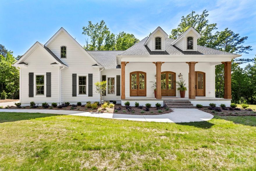 This beautifully designed 3-bedroom, 2-bath ranch combines luxury, comfort, and custom craftsmanship on an oversized 2+ acre homesite. A large rocking chair front porch welcomes you home and creates the perfect space to relax and enjoy the peaceful setting. From the moment you arrive, the gas lanterns, stained sets of double doors, and side-load 2-car garage add stunning curb appeal and timeless character. Inside, the open floor plan offers effortless flow and modern living, highlighted by premium LVP flooring throughout, designer light fixtures, custom mirrors, and upscale finishes at every turn. The spacious living areas are ideal for both entertaining and everyday living, while the high-end details and carefully selected features make this home truly one of a kind. Step outside to a private covered back porch complete with a wet bar and beverage fridge — the ultimate entertaining space for hosting guests or unwinding in your own secluded retreat. Enjoy the privacy and beauty of the expansive wooded lot while living in a home that feels both elegant and inviting.