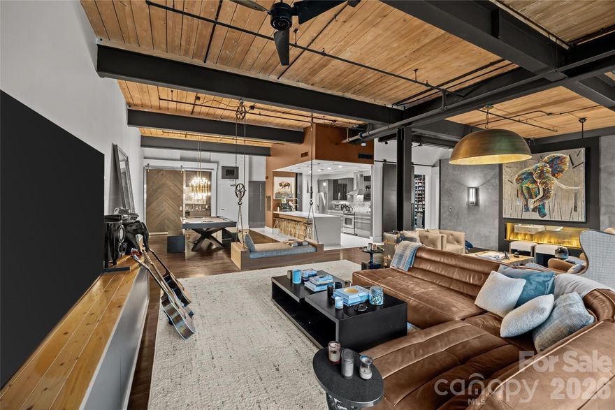 One-of-a-kind industrial loft located at The Lofts at Factory South in Charlotte’s vibrant South End, set within the iconic historic Lance Factory. This authentic adaptive-reuse conversion blends preserved architectural character with curated modern luxury, offering a rare opportunity to own a true urban showpiece.

One of the very few buildings in the city offering true live/work flexibility, the property is ideally suited for entrepreneurs, creatives, consultants, or executives seeking an integrated residential and professional environment. Monthly rentals are permitted, creating additional versatility for corporate housing, executive relocation stays, or furnished mid-term leasing.

Encompassing over 2,000 square feet, the residence is defined by soaring ceilings, exposed structural elements, warm wood planking, polished concrete accents, and expansive factory-style windows that flood the interior with natural light. Designer lighting, custom wall treatments, and bespoke finishes elevate the living experience throughout.

The open-concept living space is anchored by a dramatic two-sided linear fireplace — a striking architectural focal point shared between the main living area and the private primary suite. Framed in custom paneling and textural finishes, the fireplace creates warmth, ambiance, and visual continuity between entertaining and retreat spaces.

The chef’s kitchen pairs industrial edge with refined function, featuring sleek contemporary cabinetry, professional-grade stainless appliances, statement vent hood, full-height tile backsplash, and an expansive waterfall island wrapped in reclaimed wood with bar seating. Custom concrete countertops add durability and architectural authenticity.

Designed for entertaining and lifestyle flexibility, the residence offers a dedicated recreation lounge with billiards, designer chandelier lighting, and a fully appointed private bar with custom cabinetry. Additional fitness and training space further enhances the live-work-play environment.

The primary suite serves as a private sanctuary layered in rich textures and custom detailing, enhanced by the glow of the two-sided fireplace. The spa-inspired primary bath features an oversized walk-in shower clad in dramatic stone with rain head, handheld wand, and integrated body sprays. Custom concrete countertops continue the industrial design narrative. A boutique-style dressing room completes the retreat with extensive custom wardrobe storage, integrated laundry, curated shoe displays, and a built-in clothing steamer.

A separate guest powder room provides added convenience.

The unit includes a covered, gated parking space and private storage unit — rare and valuable conveniences for loft living.

Positioned in the heart of South End, the building offers a light rail stop at your back door with effortless access to Uptown, Dilworth, and Wilmore, along with nearby dining, nightlife, rail trail access, and daily amenities.

A truly unique and hard-to-find industrial loft offering within one of Charlotte’s most dynamic urban districts.