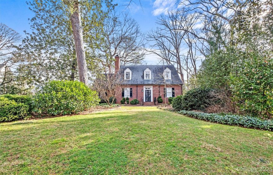 Welcome home to 2039 Queens Road East. Situated on one of Myers Park's most desirable and quiet streets, this classic cape cod brick home on a deep half acre lot boasts tall ceilings, hardwood floors and an abundance of natural light. The main level features an updated primary suite with marble tile, dual vanities and ample storage. Updated kitchen with custom cabinetry opens to the large family sunroom. The back of the house is adorned with windows connecting you to the beautifully designed and completely private terraced garden. It includes water features, and a versatile back building that includes a greenhouse and an office above. Sitting up and away from the street, this home offers traditional style, timeless beauty and a private retreat within the city.