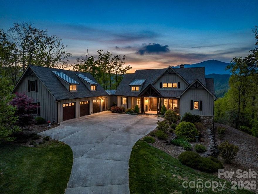 *Offered Fully Furnished* Perched against the breathtaking silhouette of the Blue Ridge Mountains, this exceptional 4.11-acre estate offers a rare blend of refined luxury and natural beauty. Designed for those who value both privacy and prestige, the home serves as a peaceful retreat where thoughtful architecture complements its rugged surroundings. A striking exterior of natural stone and classic board-and-batten siding is framed by professional landscaping that blends seamlessly into the surrounding forest, creating an immediate sense of arrival.

Inside, the home embraces its setting with organic textures and expansive windows that frame stunning seasonal views. The great room is the centerpiece, featuring soaring vaulted tongue-and-groove ceilings supported by heavy timber beams and a dramatic floor-to-ceiling stacked-stone fireplace. This inviting space flows effortlessly into a well-appointed kitchen, where rustic character meets modern convenience. Custom dark-wood cabinetry, premium stainless steel appliances, and a large granite island with an induction cooktop create the perfect setting for both everyday living and entertaining. A full covered and screened deck extends the living space outdoors.
The primary suite offers a private retreat, complete with its own vaulted timber ceiling and direct access to the screened deck. The ensuite bath is designed for relaxation, featuring a freestanding soaking tub, a glass-enclosed shower with detailed tilework, and custom wood accents that reflect the surrounding landscape. The main level also includes an additional bedroom and full bath, a private office, a walk-in pantry, and a separate laundry room.
The lower level, accessible by both elevator and stairs, provides an ideal space for recreation and guests. Polished concrete floors, a second stone fireplace, and a distinctive Coca-Cola-themed bar give the space a unique character, while two guest ensuite bedrooms offer comfort and privacy. Ample storage is available throughout. Step out onto the lower patio to enjoy the gas fire pit or hot tub while taking in the mountain views.
Outside, the property continues to impress with expansive decking, three car attached garage, and over 600 unfinished square feet above the garage ready for customization—perfect for a guest suite, studio, or additional living space.
This is more than a home—it’s a mountain retreat designed for comfort, style, and lasting connection to nature.