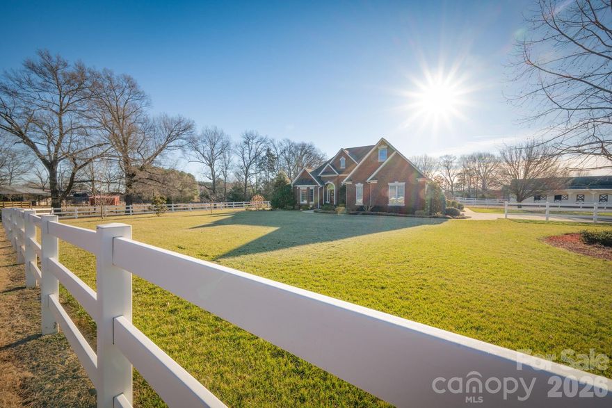 Honey Trout Farm offers an ideal setup for buyers with multiple interests. Located in the Piedmont School District at the end of a long paved driveway, this property features a well-established horse farm surrounded by similar acreage properties. Equestrian amenities include a 5-stall barn with stall mats, fans, fly mist system, walk-up hay loft, wash and tack areas, and four stalls with Dutch doors opening to the dry lot/riding area. Horses also have access to two fenced pastures with 3-board, vinyl, and/or electric fencing, one with shade trees.
The grounds are thoughtfully landscaped with established flower beds, hydrangeas, river birch trees, and a pond that adds both visual interest and a natural outdoor gathering point. A separate shop building includes a climate-controlled, finished lounge or playroom, providing flexible space for hobbies, vehicles, recreational equipment, or workshop use.
The full brick home offers expansive windows overlooking the landscaped grounds, pond, and farm areas. The split/open floor plan features a primary suite with sitting area and fireplace on one side of the home, along with an additional bedroom or office, while guest suites are located on the opposite side for privacy. Interior details include refinished hardwood floors, chair rail molding, crown molding, and columns that maintain an open yet defined layout.
Updates completed between 2015 and 2025 include refinished hardwood floors, kitchen granite countertops, appliances, roof, paver patio, HVAC systems, sump pump, lighting fixtures, water softener, and more. Convenient location with a direct route to I-485 and easy access to Monroe and Mint Hill.