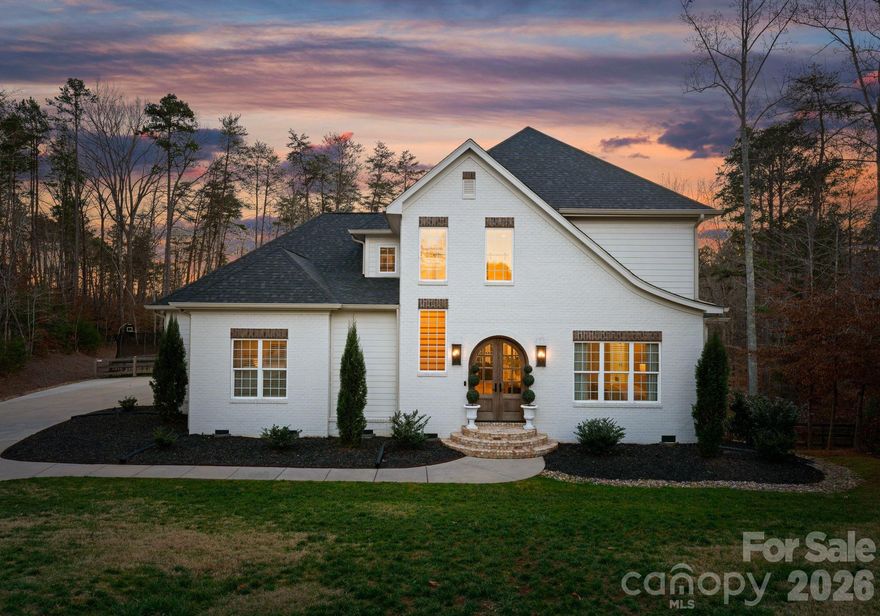 Welcome to a truly special custom home in Denver NC where thoughtful design, quality craftsmanship, and resort style living come together on a private wooded setting spanning a little over 4.5 acres. From the moment you arrive, the brick and hardie exterior, arched double entry doors, and manicured landscaping create an elegant yet welcoming first impression.
Inside, a soaring two story foyer showcases hardwood floors, custom trim, and a striking staircase with wood treads.. Natural light fills the home and highlights the open layout that flows seamlessly into the main living spaces. The kitchen is a true centerpiece featuring custom cabinetry, a large center island with seating, quartz countertops, stainless appliances, and statement lighting. Designed for everyday living and entertaining, the kitchen connects effortlessly to the dining and living areas.
The primary suite offers a peaceful retreat with hardwood floors, oversized windows, and a soothing neutral palette. The ensuite bath includes a designer vanity, bold accent wall, and a spacious walk in shower with clean modern finishes. Additional bedrooms provide flexibility for family, guests, or home office use, each thoughtfully designed with comfort and natural light.
Outdoor living takes this home to another level. A covered porch with a wood plank ceiling, ceiling fan, and stone fireplace creates an inviting year round gathering space. Just beyond, the private salt water pool (Automatic Pool Safety Cover) and expansive patio form a true backyard oasis, ideal for entertaining or quiet relaxation surrounded by trees and privacy.
Additional highlights include an outdoor kitchen ideal for entertaining, a spacious four bay garage with a fifth garage door serving a home gym, and a dedicated play area that adds functionality while maintaining the polished feel of the home. Every detail reflects intentional design and quality construction, offering a refined living experience that feels both elevated and welcoming.
