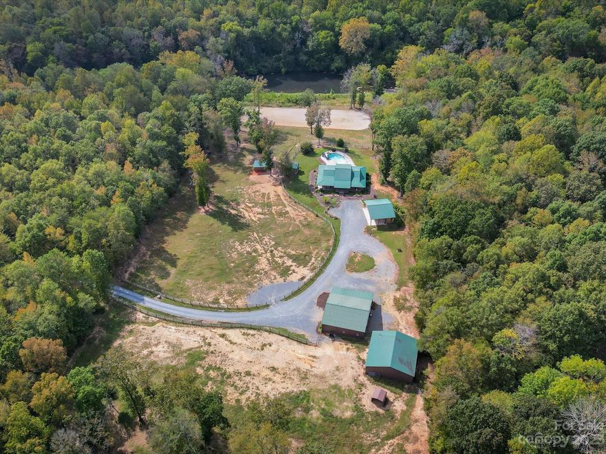 Your equestrian dreams come true at Blue Belle Farm! River-side, custom stone home tucked away on 12+ rolling acres. 2 fenced pastures and massive riding arena for your four-legged friends. Perfect amount of space in the 52'x40' 7-stall barn boasting a climate-controlled tack room, half bath, washing machine, hay loft, and feed room. For all the extras, a wired 40x40 metal storage building and 3 bay carport with workshop are essential. Metal-roofed home featuring open living area with soaring cathedral ceilings surrounded by heart pine walls. Unique horseshoe finishes in every room with hard surface flooring throughout for low maintenance. Primary bedroom features built-in vanity, custom shower, and soaker tub- perfect after a long day of riding!  Cannon ball into an inground saltwater pool with slide and beach entry. House your chickens in style with the adorable coop. This property is an ideal match for equestrian enthusiasts, hobby farmers, or anyone seeking a riverside retreat.