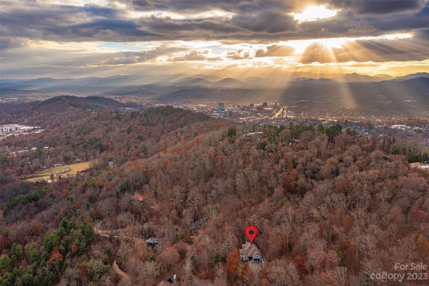 Sunrise Chateau, nestled on Town Mountain and above Chunn's Cove, features a truly unique and open floorplan that spans over three levels. Greet the Sun over long-range mountain views as light dances floor to cathedral ceiling in the great room. Enjoy coffee on one of many decks or on the screened porch with access from the primary suite. Steal a quiet moment in the upper level reading nook before setting to work in one of several potential office locations. Cozy up beside the showstopping stone fireplace or take a soak in the garden bath that overlooks the wooded 1.76 acre property. With 4 sleeping rooms, expansive entertainment room with wet bar, two car garage, new HVAC systems and roof, tons of storage space, Sunrise Chateau is a forever home. Experience private mountain living outside city limits and only five minutes to downtown Asheville.