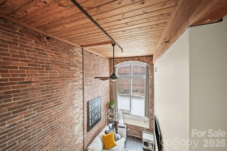 Rare 2-bedroom, 2-story loft condo for sale in Charlotte, NC — 858 sq ft of original exposed brick, soaring wood-plank ceilings, and arched factory windows inside the Historic Hoskins Mill, established 1904. This is not new construction. This is the real thing.

Welcome to Unit 129 at FoxRidge Lofts — a meticulously converted textile mill in Charlotte’s storied Hoskins neighborhood where industrial history meets modern living. Original wooden support columns, hand-hewn timber beams, and deeply textured brick walls create a space that no new build can replicate. This is the kind of place that draws people in and doesn’t let go.

The entry level opens into a sun-drenched living room framed by arched factory windows and deeply textured brick. A generous dining area connects seamlessly to a thoughtfully designed kitchen featuring white shaker cabinetry, rich granite countertops, stainless steel appliances, and room for an butcher block island — designed for the cook who understands that ambiance is half the meal. The main-floor bedroom provides drama with soaring ceilings and windows, and the full bath is finished with an espresso-toned vanity and stone countertop.

Ascend the dramatic dark-stained staircase to the upper loft — a sprawling 19’ x 17’ bedroom that feels like a private sanctuary. Exposed timber beams, original brick, and wooden ceilings make this space unlike anything else in Charlotte. It’s the bedroom you’ll never want to leave.

Beyond your unit, the building itself is an experience. Enjoy a grand community room with soaring timber ceilings and original columns, a free on-site laundry facility with no coins required, secured access, and ample parking. Google Fiber installation is projected for spring 2026, and the HOA has completed significant capital improvements in recent years, including a new fire safety system, LED lighting, parking lot upgrades, grant-funded landscaping, and a commissioned neighborhood mural. The FoxRidge Lofts community is owner-managed, engaged, and actively investing in its future. This is a place with a story — and space for yours.