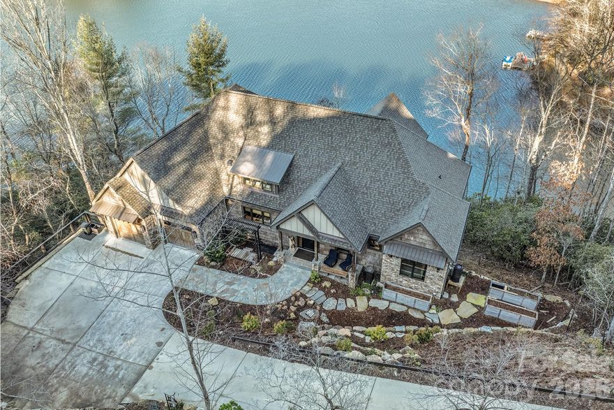 Set along the pristine shoreline of Ticoa Lake in the highly sought-after Connestee Falls Subdivision, this exceptional Arts and Crafts–inspired residence offers a rare blend of refined craftsmanship, thoughtful design, and an unmatched mountain-lake lifestyle. Built by Crone Builders and positioned on a rare double lakefront lot, the property features extensive shoreline ideal for fishing, swimming, paddling, or peaceful lakeside relaxation. Deep-water access, a private entertaining dock, and an included pontoon boat create a truly turnkey lakefront experience.

Arrival is highlighted by a concrete driveway framed by native stone retaining walls and custom wood railings, seamlessly blending into the natural surroundings. The exterior showcases rich architectural detail with native stonework, bark wood accents, and custom timber elements. A spacious double garage with custom wood doors provides ample storage and includes a Tesla charger.

Inside, the home impresses with soaring tongue-and-groove ceilings, exposed wood beams, rich hardwood floors, and solid wood doors throughout. The great room is anchored by a dramatic floor-to-ceiling native stone fireplace and expansive windows capturing tranquil lake and mountain views, flowing seamlessly to outdoor living spaces.

The chef’s kitchen is both elegant and functional, featuring an oversized Taj Mahal quartzite island, custom wood cabinetry, Wolf and Liebherr appliances, refined pendant lighting, and a custom pantry with coffee station. Open sightlines connect the kitchen, dining area, and great room—ideal for entertaining. The dining area is warm and inviting with wood-encased walls, exposed beams, and year-round views.

The main-level primary suite is a private retreat with deck access, a tray ceiling with wood detailing, a native stone gas fireplace, motorized blinds, and eight-foot solid wood doors. The spa-inspired bath features Philadelphia travertine tile, custom cabinetry with under-cabinet lighting, a spacious walk-in shower, and luxurious heated floors.

The lower level expands the living space with a generous family room centered around another floor-to-ceiling stone fireplace, custom built-ins, and access to a covered lower deck. A well-appointed wet bar with stone countertops, beverage refrigerator, and ice maker enhances entertaining. This level also includes a bonus room, a flex room ideal for office, hobby, or guest use, a dedicated fitness and wellness area with sauna and tanning bed, and over 500 square feet of workshop and storage space, providing exceptional versatility and ample room for projects and lake gear.

Outdoor living is exceptional, featuring approximately 1,145 square feet of covered, open, and screened decks, a private hot tub overlooking the lake, and a gently terraced stone path leading to the dock. Whether hosting gatherings, enjoying quiet mornings, swimming from the shore, or cruising the lake, the expansive shoreline creates a true year-round retreat.

Located within the gated community of Connestee Falls, residents enjoy access to a championship golf course, the Overlook Clubhouse with 26,000 square feet of recreational facilities, a 12,000 square foot Activity & Wellness Center with a full-time program coordinator, miles of hiking trails, tennis, pickleball, and bocce ball courts, a swimming pool with lap lanes, community organic gardens, and multiple community parks including a dog park—all just minutes from downtown Brevard.