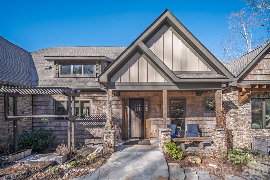 Set along the pristine shoreline of Ticoa Lake in the highly sought-after Connestee Falls Subdivision, this exceptional Arts and Crafts–inspired residence offers a rare blend of refined craftsmanship, thoughtful design, and an unmatched mountain-lake lifestyle. Built by Crone Builders and positioned on a rare double lakefront lot, the property features extensive shoreline ideal for fishing, swimming, paddling, or peaceful lakeside relaxation. Deep-water access, a private entertaining dock, and an included pontoon boat create a truly turnkey lakefront experience.

Arrival is highlighted by a concrete driveway framed by native stone retaining walls and custom wood railings, seamlessly blending into the natural surroundings. The exterior showcases rich architectural detail with native stonework, bark wood accents, and custom timber elements. A spacious double garage with custom wood doors provides ample storage and includes a Tesla charger.

Inside, the home impresses with soaring tongue-and-groove ceilings, exposed wood beams, rich hardwood floors, and solid wood doors throughout. The great room is anchored by a dramatic floor-to-ceiling native stone fireplace and expansive windows capturing tranquil lake and mountain views, flowing seamlessly to outdoor living spaces.

The chef’s kitchen is both elegant and functional, featuring an oversized Taj Mahal quartzite island, custom wood cabinetry, Wolf and Liebherr appliances, refined pendant lighting, and a custom pantry with coffee station. Open sightlines connect the kitchen, dining area, and great room—ideal for entertaining. The dining area is warm and inviting with wood-encased walls, exposed beams, and year-round views.

The main-level primary suite is a private retreat with deck access, a tray ceiling with wood detailing, a native stone gas fireplace, motorized blinds, and eight-foot solid wood doors. The spa-inspired bath features Philadelphia travertine tile, custom cabinetry with under-cabinet lighting, a spacious walk-in shower, and luxurious heated floors.

The lower level expands the living space with a generous family room centered around another floor-to-ceiling stone fireplace, custom built-ins, and access to a covered lower deck. A well-appointed wet bar with stone countertops, beverage refrigerator, and ice maker enhances entertaining. This level also includes a bonus room, a flex room ideal for office, hobby, or guest use, a dedicated fitness and wellness area with sauna and tanning bed, and over 500 square feet of workshop and storage space, providing exceptional versatility and ample room for projects and lake gear.

Outdoor living is exceptional, featuring approximately 1,145 square feet of covered, open, and screened decks, a private hot tub overlooking the lake, and a gently terraced stone path leading to the dock. Whether hosting gatherings, enjoying quiet mornings, swimming from the shore, or cruising the lake, the expansive shoreline creates a true year-round retreat.

Located within the gated community of Connestee Falls, residents enjoy access to a championship golf course, the Overlook Clubhouse with 26,000 square feet of recreational facilities, a 12,000 square foot Activity & Wellness Center with a full-time program coordinator, miles of hiking trails, tennis, pickleball, and bocce ball courts, a swimming pool with lap lanes, community organic gardens, and multiple community parks including a dog park—all just minutes from downtown Brevard.