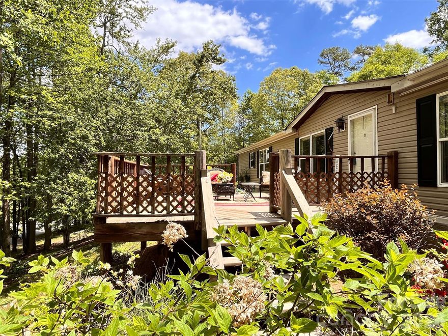 Charming country setting with one level living sitting up on the lot with great privacy.  Spacious home with two large living areas and open concept layout.  Split bedroom plan with Primary BR on one side and secondary bedrooms on other.  Huge kitchen offers abundant countertop space leading into den with gas log fireplace.  Completely updated guest bath with walk in shower.  Enjoy the large covered porch on summer days or the deck on the rear that spans the length of the entire house.  More than 1,800 s.f. of living space, all on one level!  New roof (December 2025) by Balkan Roofing.  Large recently completed detached double carport tall enough for parking an RV.  Down below the house near the street is a parking pad for a 5th wheel or additional guest parking if desired.  The community is a quiet neighborhood with excellent proximity to Asheville.  Generator and detached storage building conveys.  POA dues INCLUDE water from community system.