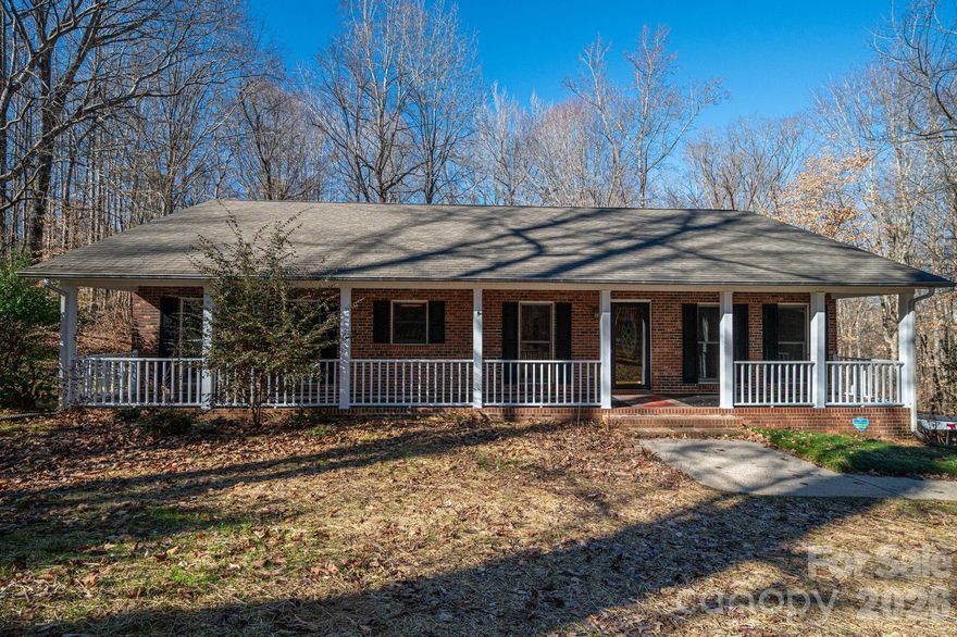 Surrounded by 8.6 wooded acres, this home offers a peaceful, private setting with a welcoming full-length front porch. This three bedroom/2 bath home has a split floorplan. The living room features a large brick fireplace with gas logs and a back door leading to a screened porch overlooking the property. Kitchen includes a breakfast area and bar, creating a functional layout for everyday living. A full unfinished basement offers high ceilings, a wood stove, two garage doors, and abundant storage. Additional storage is available in the backyard outbuilding. The seller previously added additional foundation support. Portions of the land are in a flood plain. Recent interior updates include new carpet in all bedrooms, fresh paint in several rooms, and a new hot water heater installed in December 2025. In the past month, the sellers completed extensive maintenance and improvements, including installation of a French drain line in front of the home, repairs to the front porch, leveling the concrete and painting porch and porch floor. Gutter cleaning, installation of a drainpipe and sealed wall on the left side of the home, driveway and sidewalk pressure washing, reseeding of the front yard, construction of a berm around the front and side of the home. A screened back porch, deck area, basement storage, and expansive acreage make this property a great opportunity for those seeking space, privacy, and long-term potential. Items that need to be repaired are: No cap on chimney, 1 garage door in need of repair, exterior outlets not working and need covers, laminate floor peeling in some spots, broken seal on window in living room, range has broken door hinge and broken front glass, guest bathroom is missing sink stopper. The power of attorney for the seller has never lived in the home.