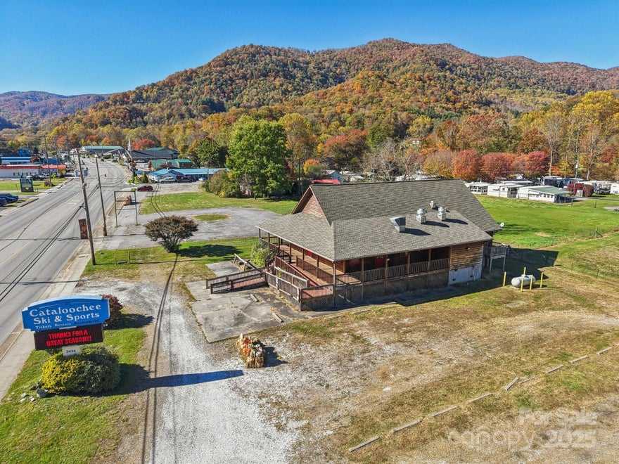 Incredible opportunity to own a versatile commercial building in the heart of the Central Business District of Maggie Valley! This expansive 2,800+ square foot property sits on a generous 0.88-acre lot and is packed with features ideal for a variety of retail or service-oriented business ventures. The building offers a spacious open floor plan, making it easy to customize for your specific use. Whether you're envisioning a boutique, art gallery, café, brewery, or professional office space, this location checks all the boxes. The building has been used as a restaurant in the past, and the property already includes walk-in coolers, restrooms, and an office area – reducing your build-out time and costs. Enjoy the charm and functionality of a covered wraparound deck, perfect for seating, customer gathering, or product display. There's also a large parking area that adds significant convenience for customers and staff alike. The building features ramp access to the main level, supporting easy entry for all. High visibility is guaranteed with a prominent commercial sign plus an electronic message sign – both of which convey with the sale. Situated along the bustling Soco Road corridor, this property enjoys strong daily traffic and great exposure to tourists and locals year-round. The back portion of the lot lies within a floodplain; however, it remained unaffected even during Hurricane Helene, demonstrating its resilience. With great bones, prime location, and flexible zoning, this is your chance to bring your commercial vision to life in one of Western North Carolina’s most visited mountain towns!