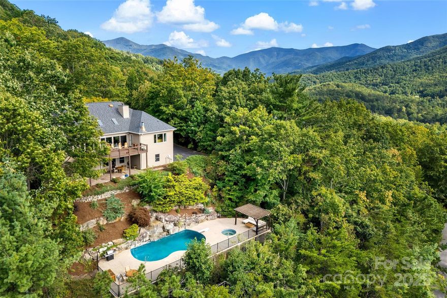 An amazing view of Black Mountain and the Swannanoa Mountain Range greets all who come here. This spacious home is just a few minutes from downtown Black Mountain with easy access, plenty of level parking, and with unobstructed views that are some of the best available. Main level entry allows one level living if desired, with 3BR, 3BA, Kitchen, Living Room, and Laundry all on the main floor. The Living Room, Sitting Area and Dining Room are part of an open floor plan with vaulted ceilings, a fireplace, skylights, and a panoramic sliding patio door flowing out onto the deck. The deck is excellent for entertaining and relaxing. In the Kitchen you'll find quality oak cabinetry, a gas cooktop, a wall oven, a built in microwave, and a warming drawer. There is seating for two at the island which casually blends into the breakfast area with larger seating...and great outdoor views from it's large windows. The primary BR also has great views, a fireplace, and a separate door onto the deck.  Downstairs, you will find an additional Family Room with a fireplace, a large Bedroom, a Full Bath, an Office, a Flex Room, a 2 car Garage, and a Workshop that also has an outside entrance. 
For a change of pace and to spend time outside, stroll down the large granite steps through the landscaped forest edge to the swimming pool. Into the pool a waterfall flows the over the massive and artfully constructed boulders. It is both beautiful and soothing any time of day or evening. The pool deck has plenty of room, and includes a pergola. The cabin style Pool house can be used for many things including changing, and also has a .5 Bath. This property has some of the best views you'll find. It is easily accessible from town, has spacious living quarters, and includes a pool with a waterfall. All in all, a very rare find.