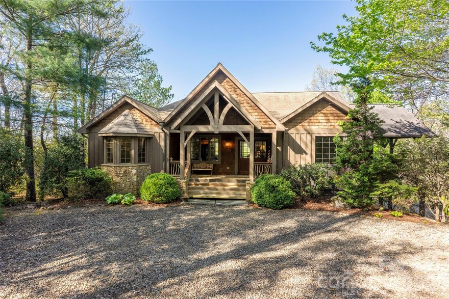 A private mountain estate property nestled on Hawk Mountain with over 2 acres of sweeping views of Lake Toxaway and the surrounding mountains. Inside, the home is warm and inviting, centered around a stunning great room with a stone fireplace, a chef’s kitchen, and a dining area highlighted by rich wood architectural details. These spaces flow seamlessly onto an expansive covered deck designed for entertaining, complete with a barbecue area, lounge seating, and an outdoor fireplace. In addition to the charming main level, a lower level offers a spacious media and game room and three additional bedrooms. The grounds are just as impressive, featuring lush perennial gardens, terraced stone landscaping, and ample guest parking. There is so much to enjoy in this peaceful mountain retreat.