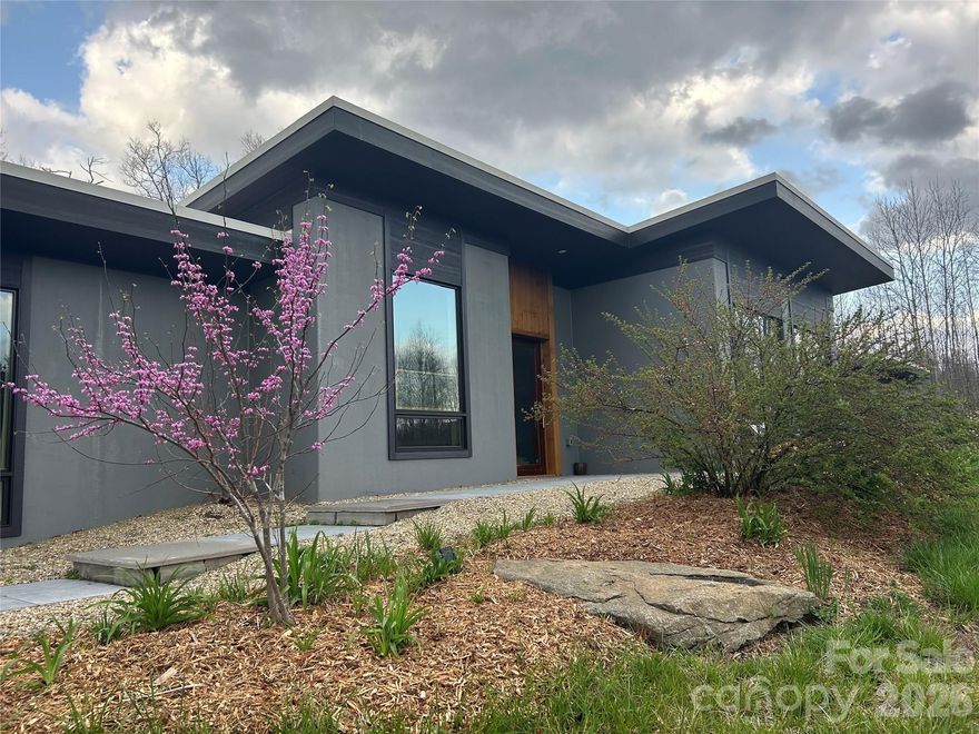 Modern Net-Zero Luxury in Asheville. Located in the eco-community of Green Acres, this custom-built home combines modern design, sustainability, and convenience— just 3 miles from Whole Foods, Ingles, restaurants, and more. Built as a true net-zero residence, it produces more energy than it consumes with a 6.8 kW solar array, Bosch 18 SEER HVAC, Blaze King wood stove, heat pump water heater, and R-30 insulated concrete walls. A continuous white membrane roof (95% reflective) further enhances efficiency.
Inside, the great room impresses with soaring ceilings and exposed I-bearms. Solid oak and mahogany doors, hurricane-rated laminated glass windows, and polished concrete floors designed for passive solar warmth reflect exceptional craftsmanship. The chef’s kitchen features European cabinetry, granite counters, Grohe faucet, Miele dishwasher, Liebherr refrigerator, wine cooler, and a welcoming bar niche.
The primary suite offers a spa-like bath and huge walk-in closet with European drawers. A Jack-and-Jill suite adds walnut cabinetry, German fixtures, and fine tile work. 
Outdoor living includes two patios- one off the kitchen and one off the master— plus gardens, fruit trees, a fire pit, and natural stone accents. Set on one acre with the option to add two more for privacy, this home offers an unmatched balance of modern luxury, energy independence, and Asheville living.