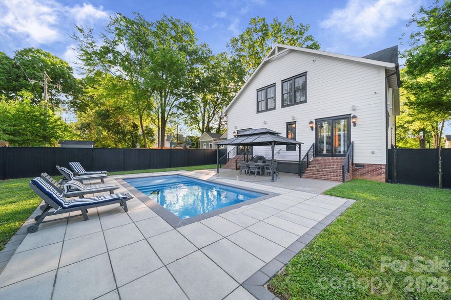 Sophisticated Southern charm meets low-maintenance luxury in this 4-bedroom, 3.5-bath Charlotte home — walk to Midwood dining and the Lynx Light Rail from this quiet dead-end street. A striking wrought iron entry door opens to 10-ft ceilings and rich oak hardwoods flowing throughout 2710 square feet. The GE Monogram kitchen is appointed with a gas range, hand-laid brick backsplash, integrated beverage bar, and an oversized quartz island designed for both function and gathering. The living room, anchored by a gas fireplace, opens seamlessly to the heated pool and patio. The main-level primary suite is a true retreat with direct pool access, a custom closet, dedicated vanity, and a spa-caliber bath. Dining, laundry, and a powder room complete the main level.
Outdoors, a 12x25 heated pool (2023) anchors an expansive patio with dedicated gas connections for a grill and fire pit, wrapped in powder-coated Ultra Aluminum privacy fencing — a refined and  low maintenance setting. Integrated audio runs throughout the main level, garage, and pool area. Upstairs, 9-ft ceilings enhance three bedrooms, two designer baths with brick and marble finishes, generous walk-in closets, city views, and a second laundry. The home's standout feature is a fully self-contained 700 sq ft suite with its own private entrance, full kitchen, living area, bedroom, full bath, and in-unit laundry — ideal as extra living area, a guest suite, income-producing rental, home office, or fitness studio, with the option to connect to the main home or remain completely independent.
Built with intention: Front irrigation, 3-zone HVAC with a dedicated suite zone, tankless water heater, CPI security system with cameras, designer plantation shutters, wrought iron interior staircase, no-maintenance aluminum trellis and railings, triple-wide driveway, and an extra-deep 2-car garage with utility sink. Washer/dryer new 2024. Exterior painted 2021. Move-in ready.