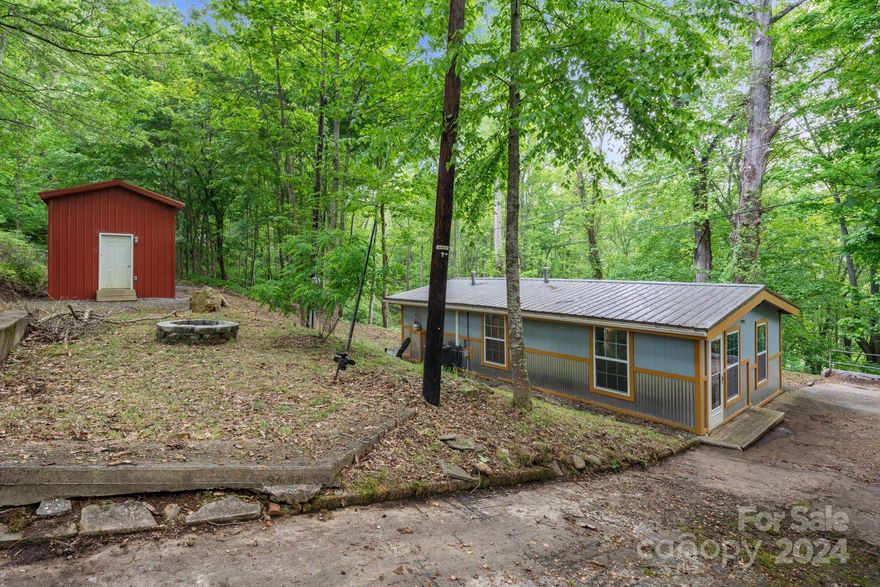 Vintage mountain getaway just a short trip from downtown Waynesville NC. Surround yourself with lush nature, wildflowers, and seasonal mountain views in this low-maintenance, no HOA, furnished mountain property. Retro kitchen appliances provide a sense of style and flair in a one-level paradise. Listen to the rain on the metal roof as you lounge in the garden bathtub, and enjoy peace of mind with a whole house humidifier, radon mitigation unit, HVAC, and well-maintained septic tank. Take your coffee on the porch while basking in views of the mountains and abundant hardwoods. Host your friends by the fire pit, and enjoy the convenience of the 372 sq ft insulated barn, complete with electricity, ventilation, and a dedicated gravel driveway. This property offers 2 parcels, providing for future division, or enjoy a larger lot all to yourself. Stellar STR opportunity, vacation home, or primary residence! Enjoy peace, privacy, and convenience in this uniquely perfect property.