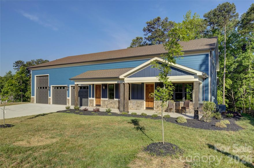 Experience the perfect fusion of luxury living and functional design in this one-of-a-kind custom Barndominium, where rustic modern style meets unmatched versatility. A welcoming covered rocking chair front porch sets the tone, leading into a bright, expansive open-concept great room that seamlessly blends the dining area, chef’s kitchen, and family room across the entire length of the home. The thoughtfully designed kitchen features sage cabinetry, leathered-finish granite countertops, a gas range with an exhaust hood, and a spacious island with a farmhouse sink, while a butler’s pantry with a beverage station and built-in wine rack adds convenience for entertaining. Sliding glass doors open to a covered deck with a rich wood plank ceiling and fan, perfect for year-round enjoyment. The main-level primary suite offers a private retreat with dual vanities, brick-look tile flooring, and an oversized shower, while a nearby laundry room and work area enhance everyday efficiency. Upstairs, three generously sized bedrooms include a private en suite and a shared hall bath. A large loft/flex space ideal over the garage for entertaining, with an overlook of the showpiece garage. Car enthusiasts and hobbyists alike will appreciate the impressive 2,000+ sq ft three-bay garage with showroom flooring, perfectly suited for collections, boats, or workshops—making this home a rare opportunity to combine elevated living with an expansive workspace all under one roof.