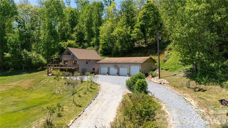 What a beautiful, peaceful mountain setting, this property offers the kind of privacy and usable outdoor space that is getting harder to find. The home sits overlooking a wide open yard and the Toe River with wooded surroundings, creating a quiet retreat while still offering plenty of room to enjoy the outdoors. Did I mention you have a recreational easement to the river? Well you do! A large wraparound deck gives you the perfect place to entertain guests, grill out, or simply sit back and take it easy. The covered portion of the deck provides year-round outdoor usable space and adds even more functionality to the home. The elevated position of the house allows for beautiful views across the property while still maintaining privacy from neighboring homes.
The exterior also features a spacious detached multi-bay 1,500 sq.ft. garage with ample room for vehicles, equipment, workshop space, recreational toys, or additional storage. The wide gravel driveway offers easy access, abundant parking, and plenty of room for guests or trailers. Beneath the home, additional covered space provides even more storage opportunities for outdoor gear and equipment. Inside the kitchen that was thoughtfully designed for both everyday living and entertaining. The spacious layout offers an abundance of countertop space, wood cabinetry, and a large center prep and seating area that naturally becomes the heart of the home. Features updated stainless steel appliances, including a French door refrigerator, sleek vent hood, dual wall ovens, dishwasher, and smooth cooktop perfectly positioned beneath a custom tiled backsplash that adds texture and character throughout the space. Modern cabinetry with frosted glass accents provides a clean contemporary look while still keeping the home warm and inviting. A large double basin sink sits beneath a picture window overlooking the covered outdoor area and surrounding greenery, making even everyday tasks feel relaxing. The extensive counter space and smart layout make cooking, hosting, and gathering easy and functional. Recessed lighting and stylish fixtures complete the kitchen while adding to the comfortable atmosphere of the home. Inside the garage you will find a vehicle lift already installed, making it ideal for automotive work, maintenance, hobby projects, or extra vehicle storage. The high ceilings and wide access doors allow for comfortable maneuverability and create a practical workspace for everything from everyday use to serious shop work. The garage is positioned conveniently beside the home with easy access from the large gravel driveway, providing abundant parking and room for trailers, ATVs, boats, or guests. This is the kind of detached garage setup that is increasingly hard to find and adds tremendous value and versatility to the property.
Whether you enjoy cooking for family, entertaining guests, or simply enjoying a quiet morning coffee with natural views all around, this kitchen delivers a blend of style, function, and comfort that is hard to find. Please no drive-bys. Owners are asking for a 1 day notice before showing.