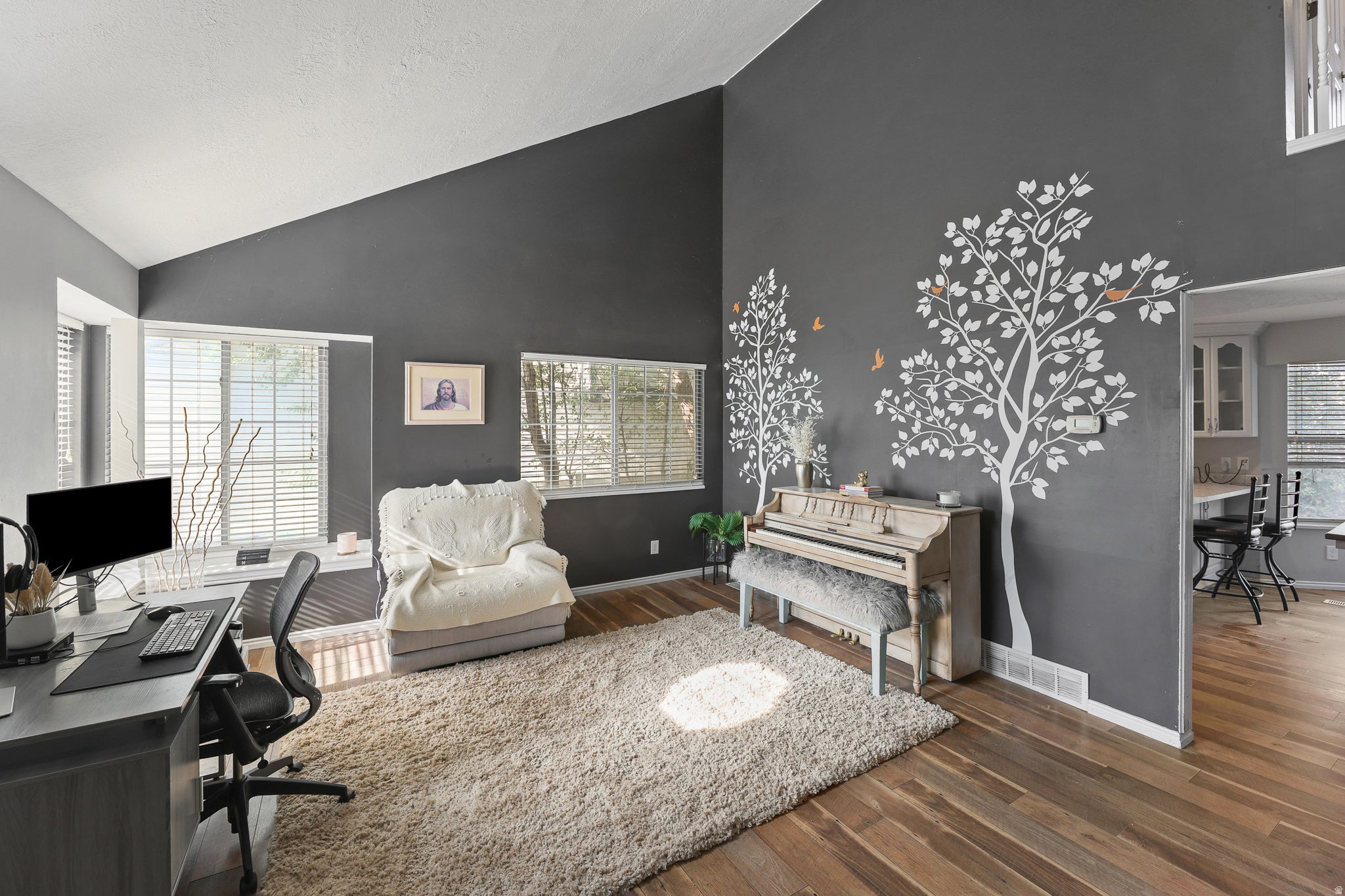 Vaulted ceiling, wood-finish flooring, multiple windows with blinds, architectural wall accent