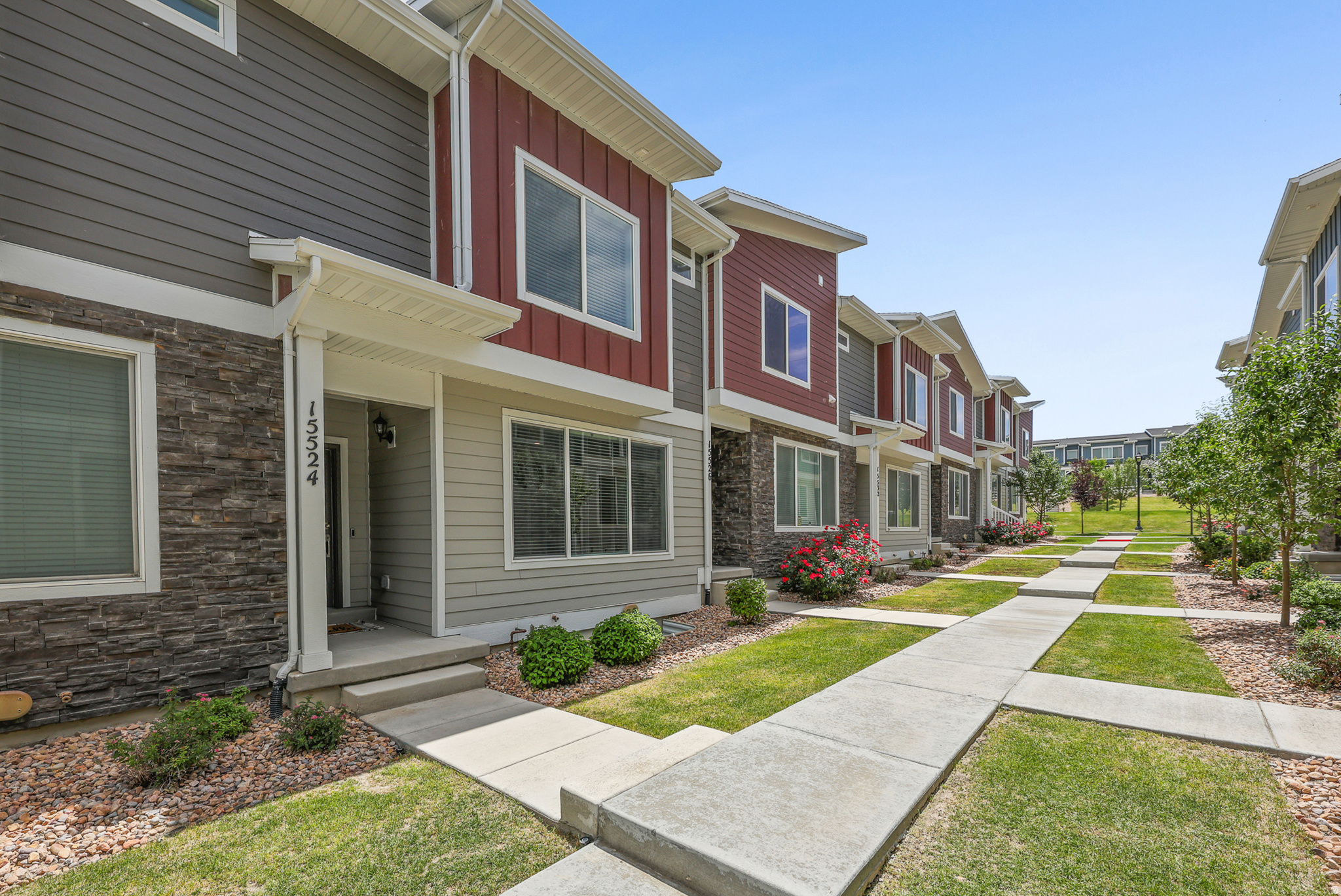 Contemporary townhouse exterior featuring a covered entry, stone veneer accents, horizontal siding, and a concrete walkway