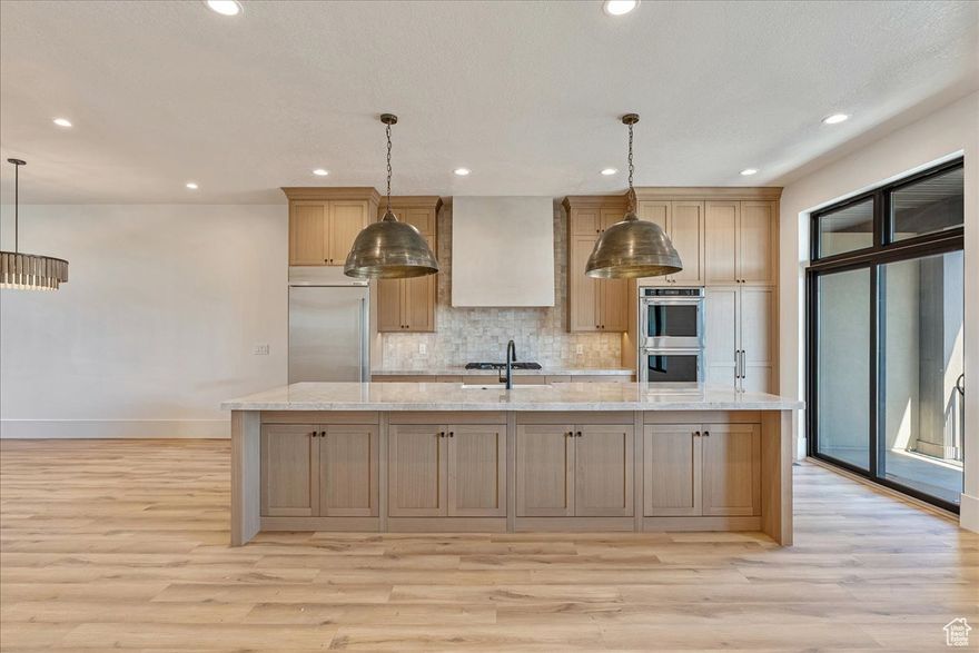 Welcome to this stunning luxury townhome that masterfully blends elegance and functionality all in one! Featuring an open-concept floor plan, this home boasts a spacious kitchen outfitted with custom cabinetry, a large center island with  Quartzite countertops, designer pendant lighting, and high-end stainless steel appliances including a gas cooktop and double wall ovens. The rich wood tones and soft neutral finishes create a warm, timeless aesthetic. Enjoy indoor-outdoor perfect for entertaining. The main living area is adorned with wide-plank luxury flooring, custom lighting, and recessed ceiling fixtures to highlight the home's modern charm.