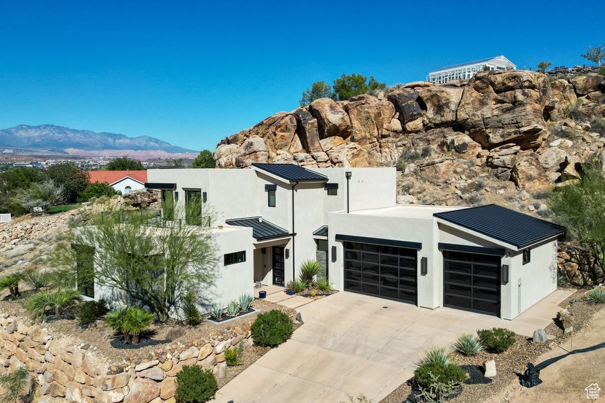 Experience modern luxury in this custom-designed masterpiece by Wayne Andersen Custom Homes, nestled on a rare 1.02 acre lot with jaw-dropping mountain views and direct access to ancient Indian petroglyphs etched into the natural rock formations behind the home right on your property. Step through the dramatic steel-and-glass front door into a light-filled interior boasting large format porcelain tile, expansive metal-framed windows that capture the stunning surroundings, and a floating wood and metal staircase. Built with quality and longevity in mind, this home features 2x6 construction and blown in insulation, ensuring enhanced energy efficiency and year-round comfort. The chef's kitchen impresses with high-end Bosch appliances (including a microwave drawer and refrigerator), a waterfall-edge Bianco Antico granite island, Arctic White quartz countertops, gray glass subway tile backsplash, and rich horizontal-grain cabinetry. Overhead, open beams and sleek steel elements lend a modern yet warm aesthetic. The open-concept living area features a contemporary tile gas fireplace, a recessed TV niche, and is wired for sound with indoor and outdoor speakers perfect for entertaining or relaxing to your favorite music. Even better, all audio equipment is included, offering a truly turnkey experience for media lovers. The primary suite is a private sanctuary, thoughtfully designed to maximize comfort, style, and connection to the stunning natural landscape. Wake up each morning to panoramic views of dramatic red rock formations and surrounding mountains, visible through expansive windows and from your spacious private patio the perfect spot to enjoy coffee at sunrise or unwind under the stars. Inside, the suite showcases premium finishes and modern touches, including a custom walk-in closet with built-in drawers and shelving for effortless organization. The spa-inspired en suite bathroom features a sleek double sink vanity, designer fixtures, and a luxurious walk-through shower with dual shower-heads offering both elegance and functionality. The guest en-suite also includes a spa-like bathroom with double sink vanity, walk-in shower, built-in closet shelving, and stunning views from the room. Outside, the xeriscaped backyard is an entertainer's dream, featuring a custom sauna, a built-in Char-Broil BBQ, a cozy fire pit, and solar-powered landscape lighting. Relax and explore your private outdoor space with natural boulders and red rock cliffs as your backdrop. The oversized garage features epoxy-coated floors, tinted glass & metal doors, and extra-tall ceilings-perfect for storing recreational equipment, vehicles, or setting up a workshop.  Located in a secure gated community, this home is ideally positioned within a short distance to the following trails: Radio Tower trail, Kentucky Lucky Chicken trail, and trailhead for the Virgin River bike path. The home is a short drive from the towering cliffs of Zion National Park, the hoodoos of Bryce Canyon, Snow Canyon State Park and the North Rim of the Grand Canyon. Explore world-class hiking, mountain biking, and water-sports at four nearby reservoirs. The region is also known for its internationally renowned golf courses that have hosted the PGA tournament and the LPGA. Saint George is also the host for many events such as the Ironman, Red Bull Rampage, The Huntsman Senior Games and the Saint George Marathon.  All information provided is reliable but not guaranteed. The buyer is responsible for verifying all listing details, including square footage and acreage, to their own satisfaction.