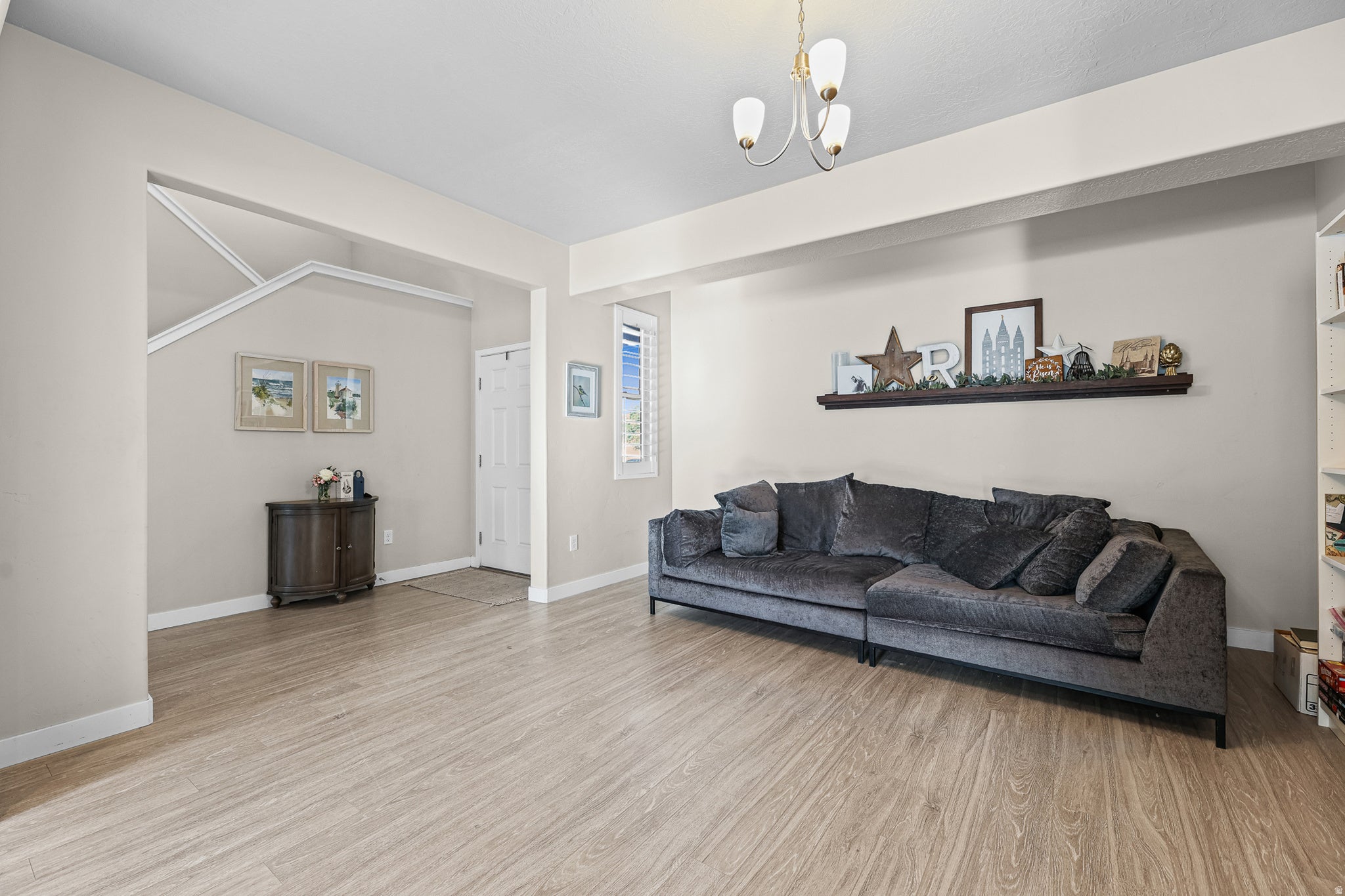 Bright living area featuring wood-finish flooring, a built-in wall shelf, and a multi-pane window with plantation shutters