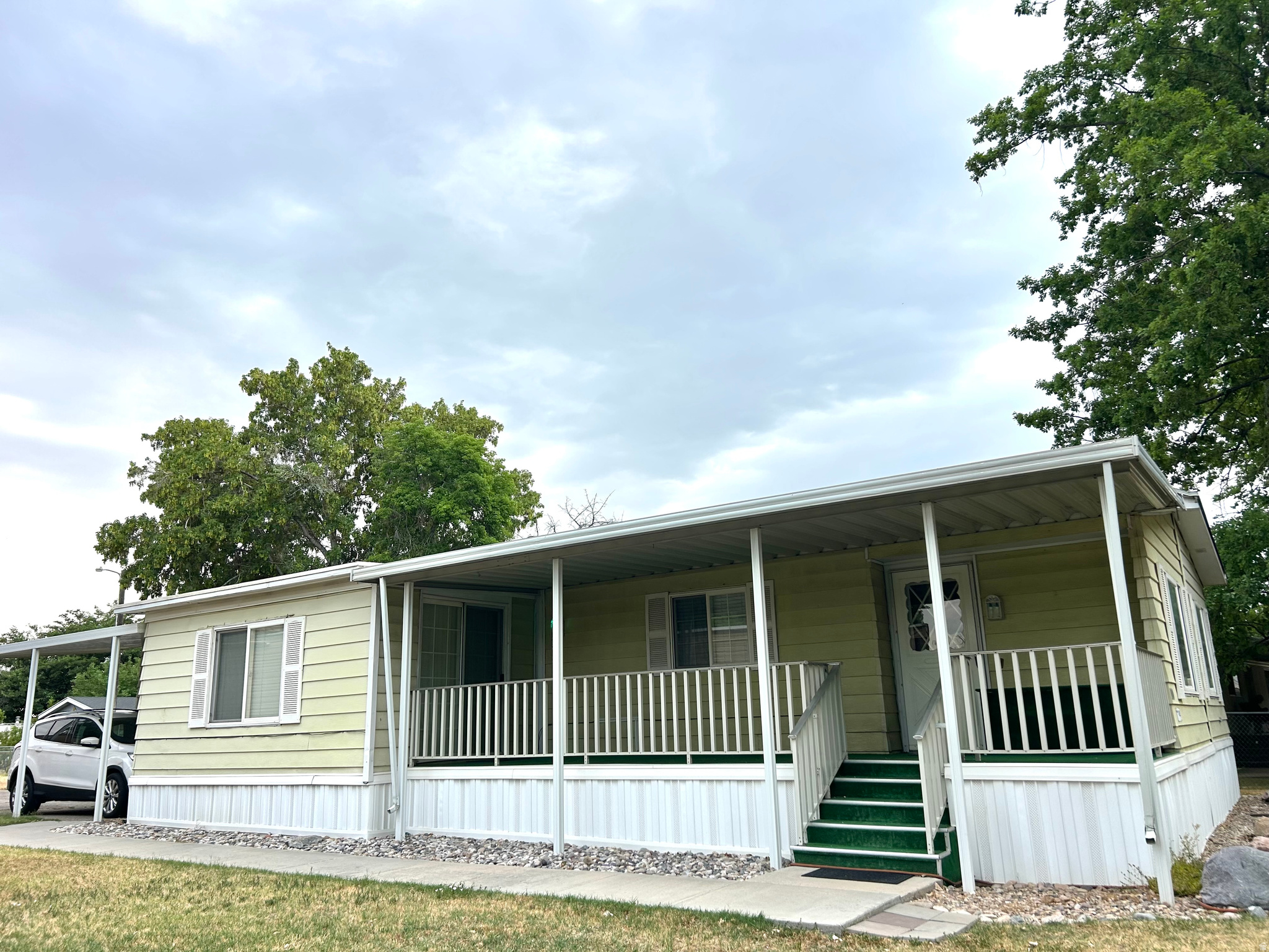 Single-story residence featuring a covered front porch with white railing, a separate covered carport, light-colored siding, and white window shutters